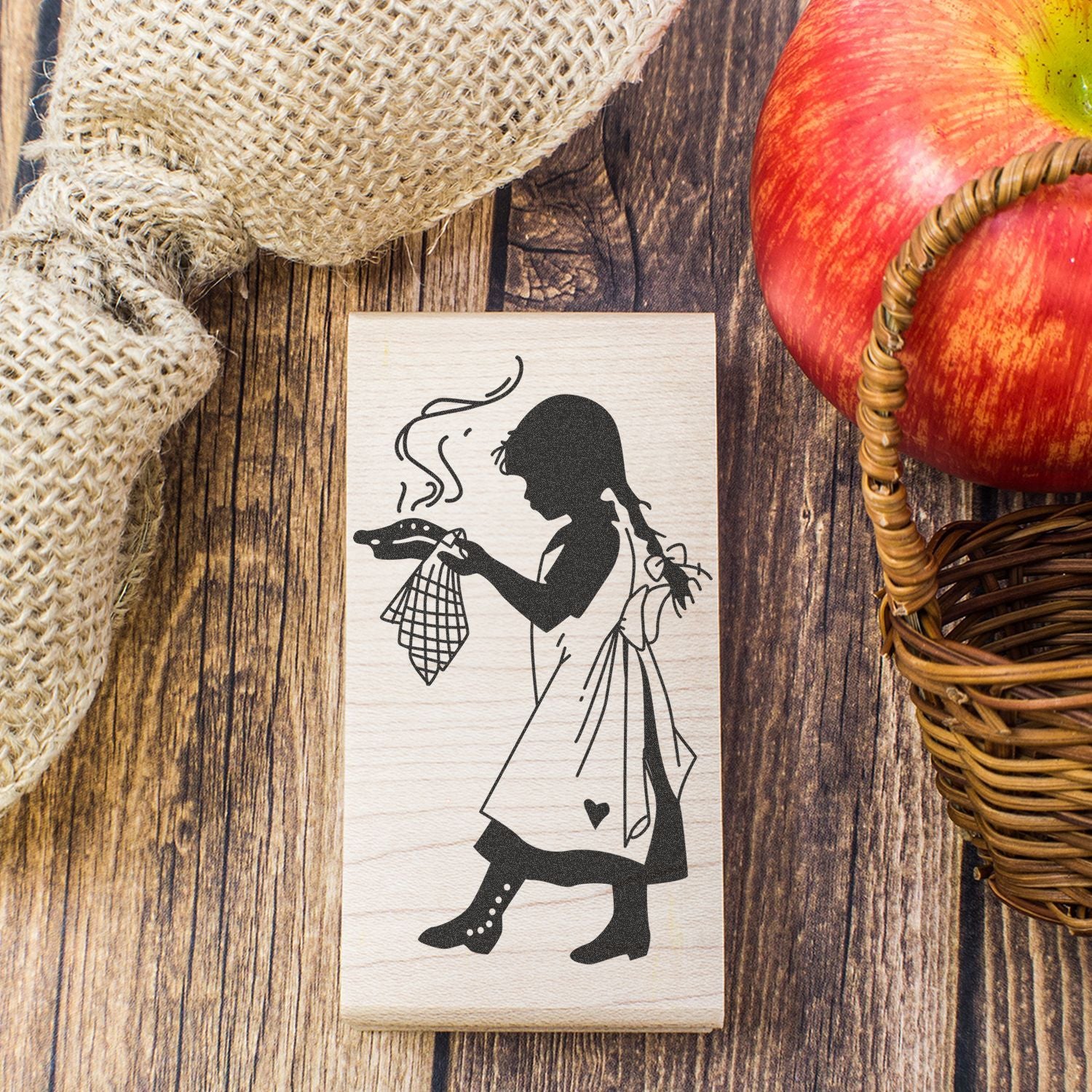 Rustic wooden stamp with girl silhouette holding apple, fall farmhouse decor on wood background with burlap and basket apple.