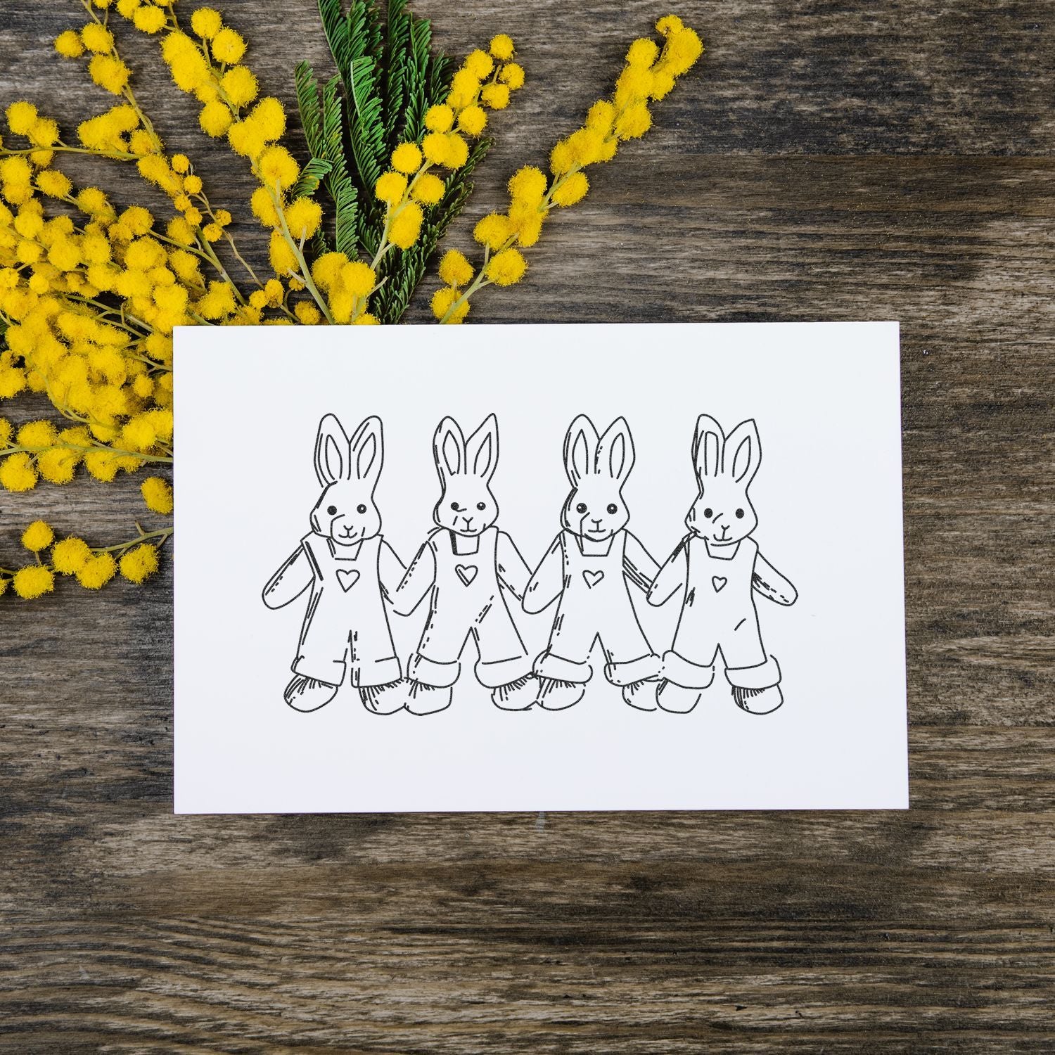 Hand-drawn Easter bunny card with yellow mimosa flowers on rustic wooden background.