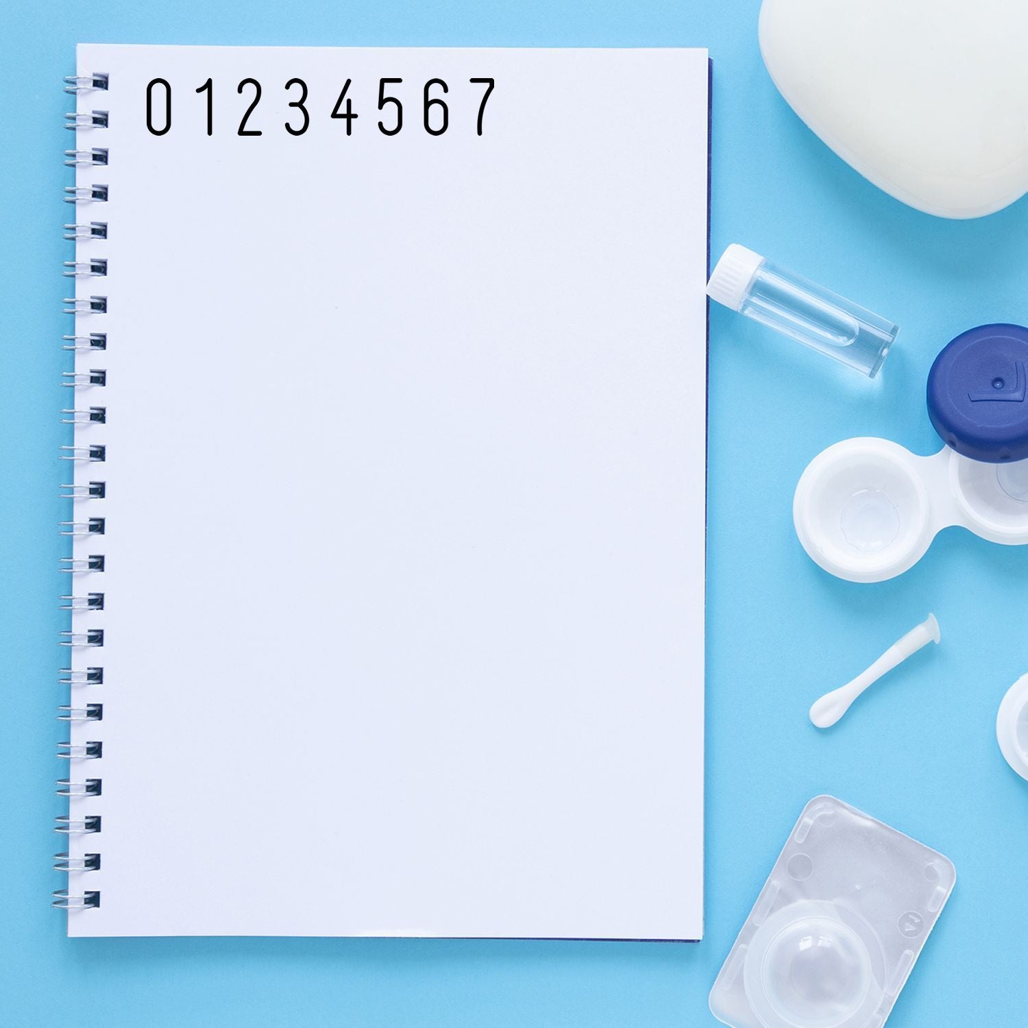 Blank spiral notebook with contact lens care supplies, solution vial, and lens cases on a blue background.