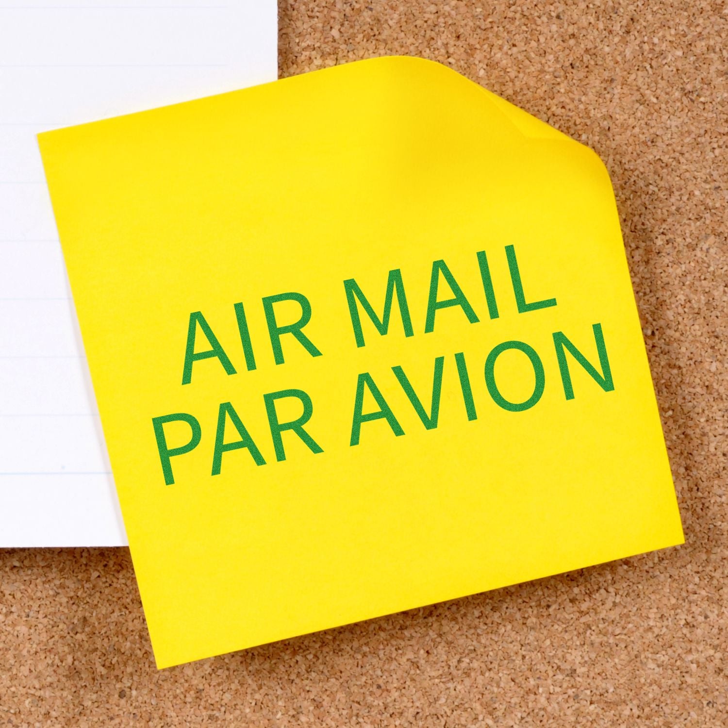 Air mail Par Avion label on yellow note pinned to cork board, indicating international air shipping.
