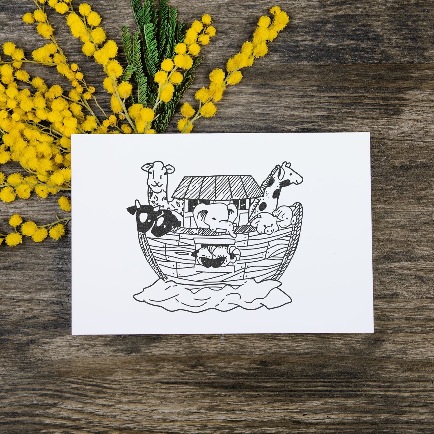 Noahs Ark animal illustration card on rustic wood with yellow mimosa flowers, black and white hand-drawn line art greeting card.