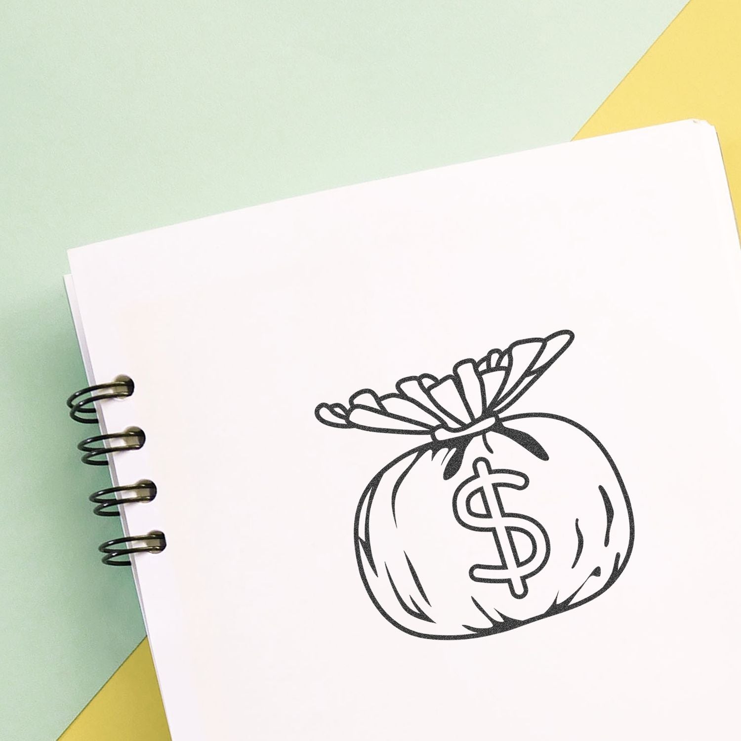 Spiral notebook with money bag and dollar sign illustration on a pastel green and yellow background.