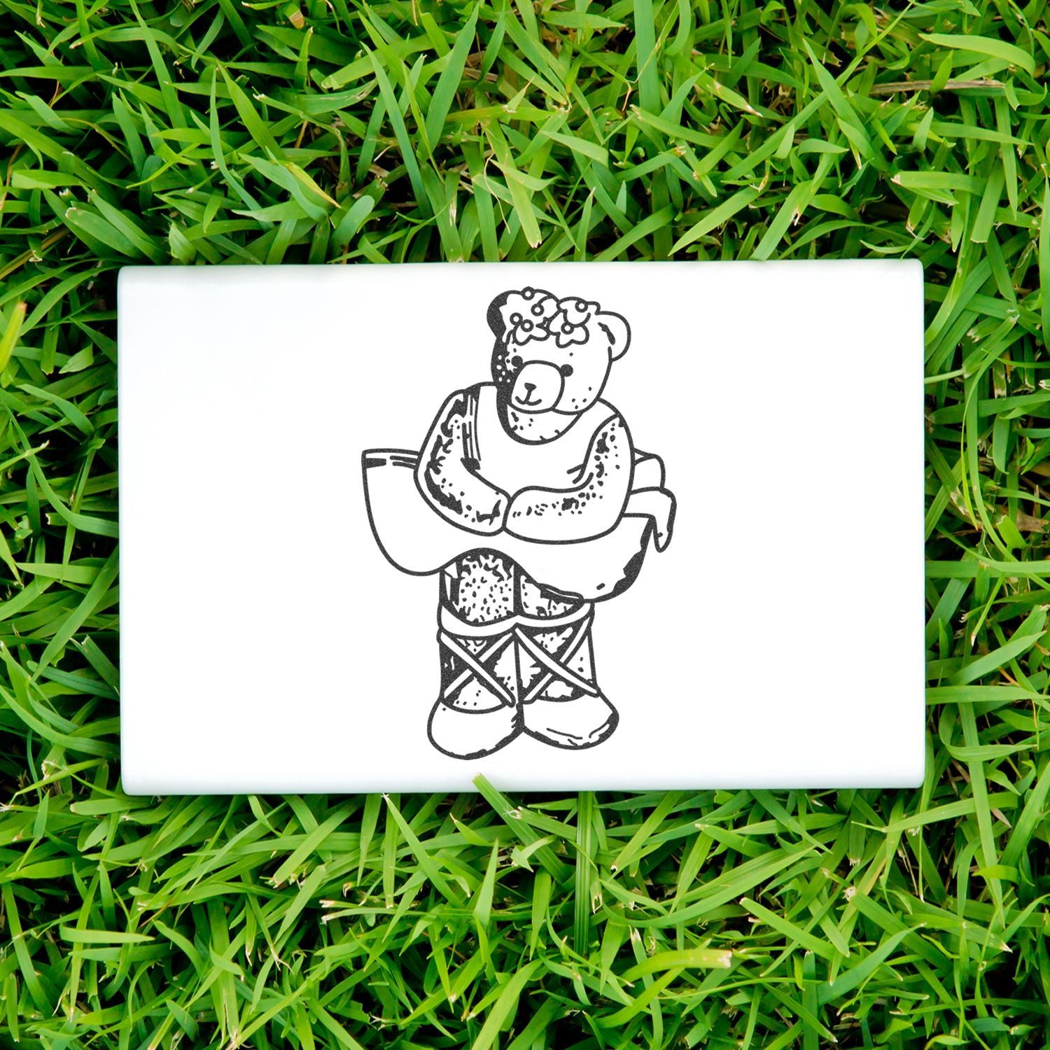 White ceramic tile with cute teddy bear line art on green grass, decorative home or garden decor.