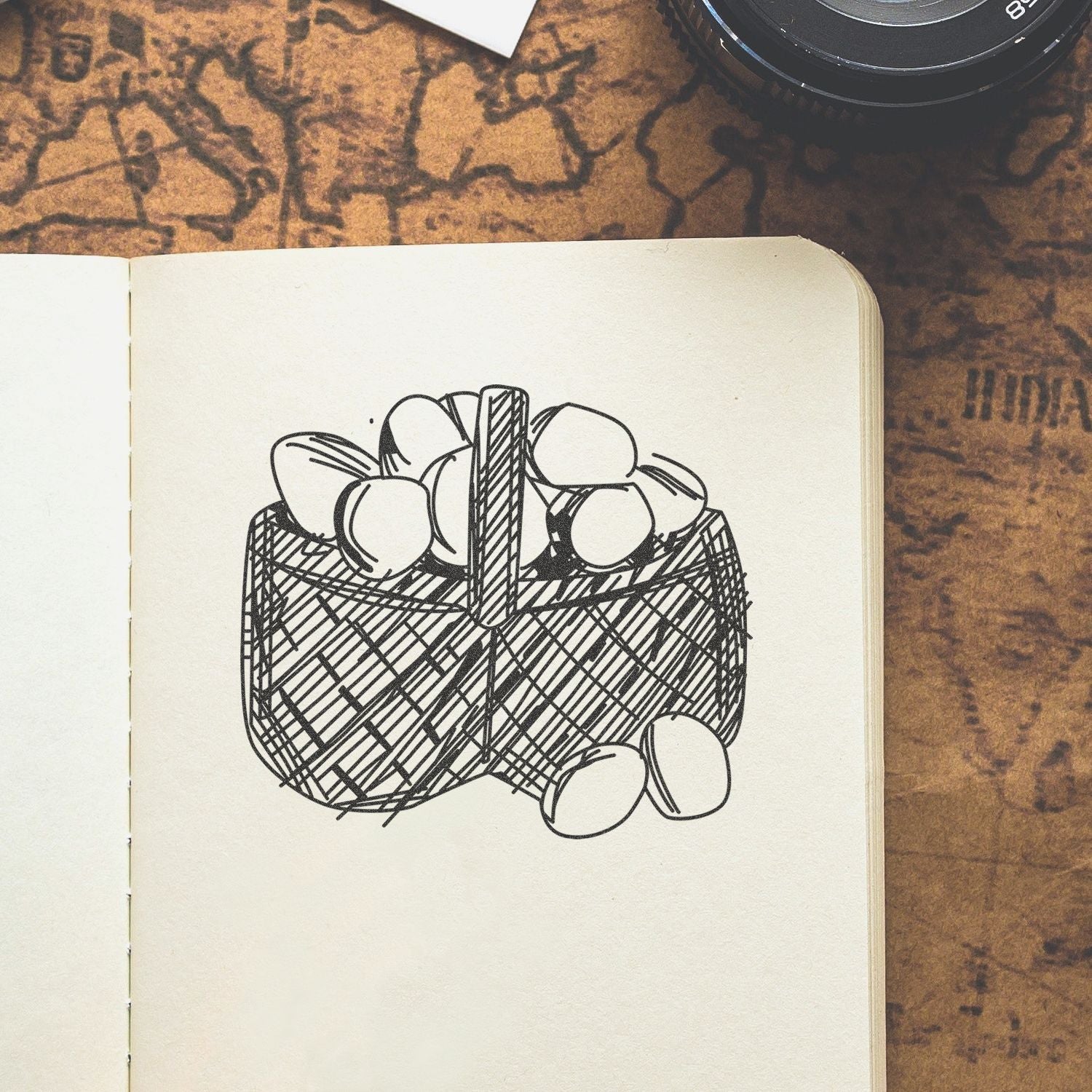 Open sketchbook with hand-drawn basket of eggs on a rustic desk, with a camera lens in the corner
