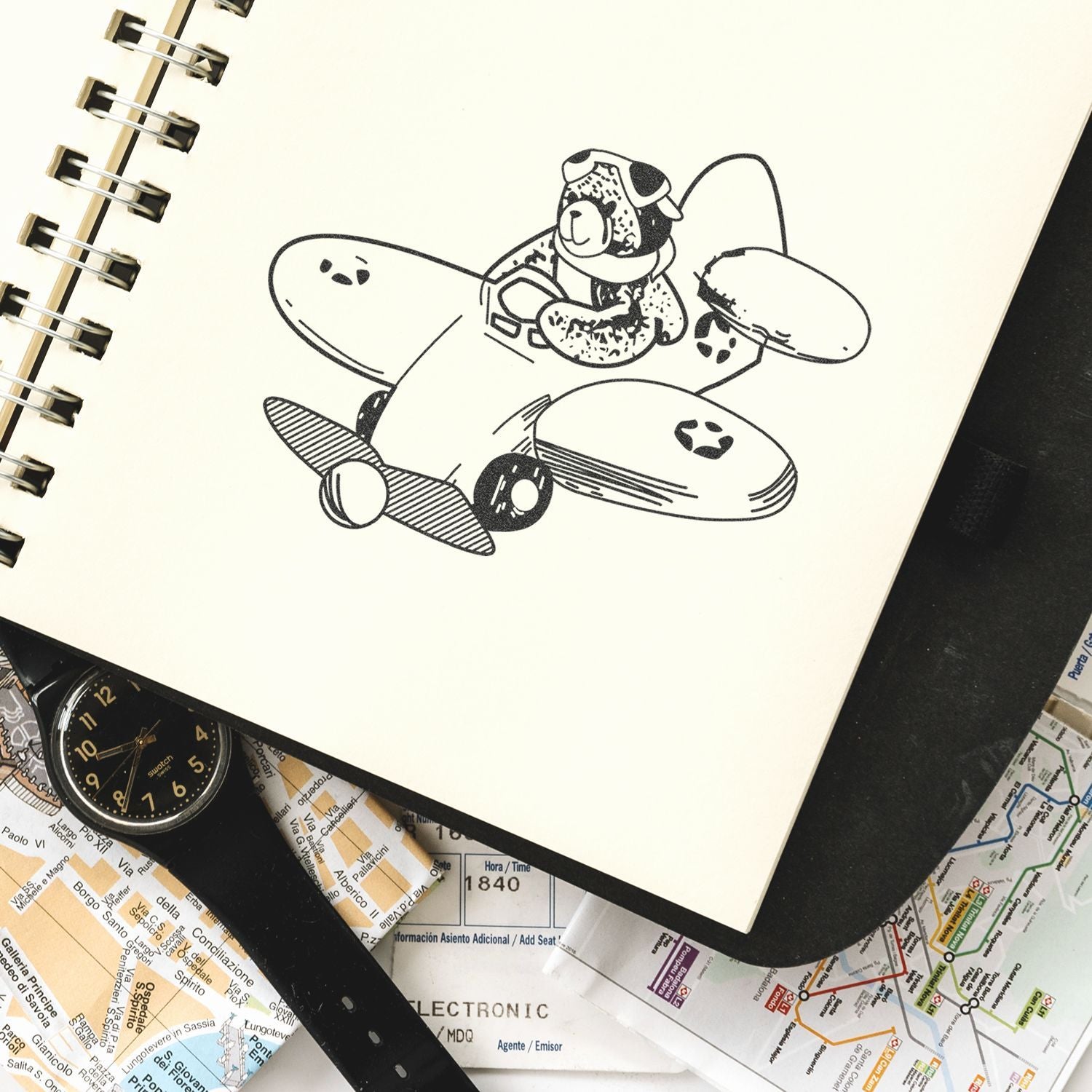 Sketch of a dog riding an airplane in a spiral notebook, surrounded by travel maps and a wristwatch.