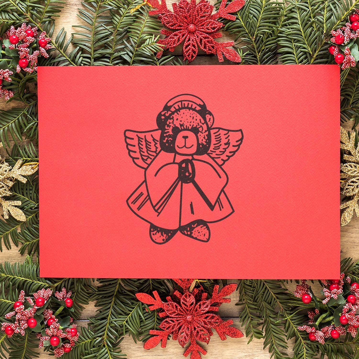 Red Christmas greeting card with an angel teddy bear design, surrounded by festive holiday greenery and decorations.