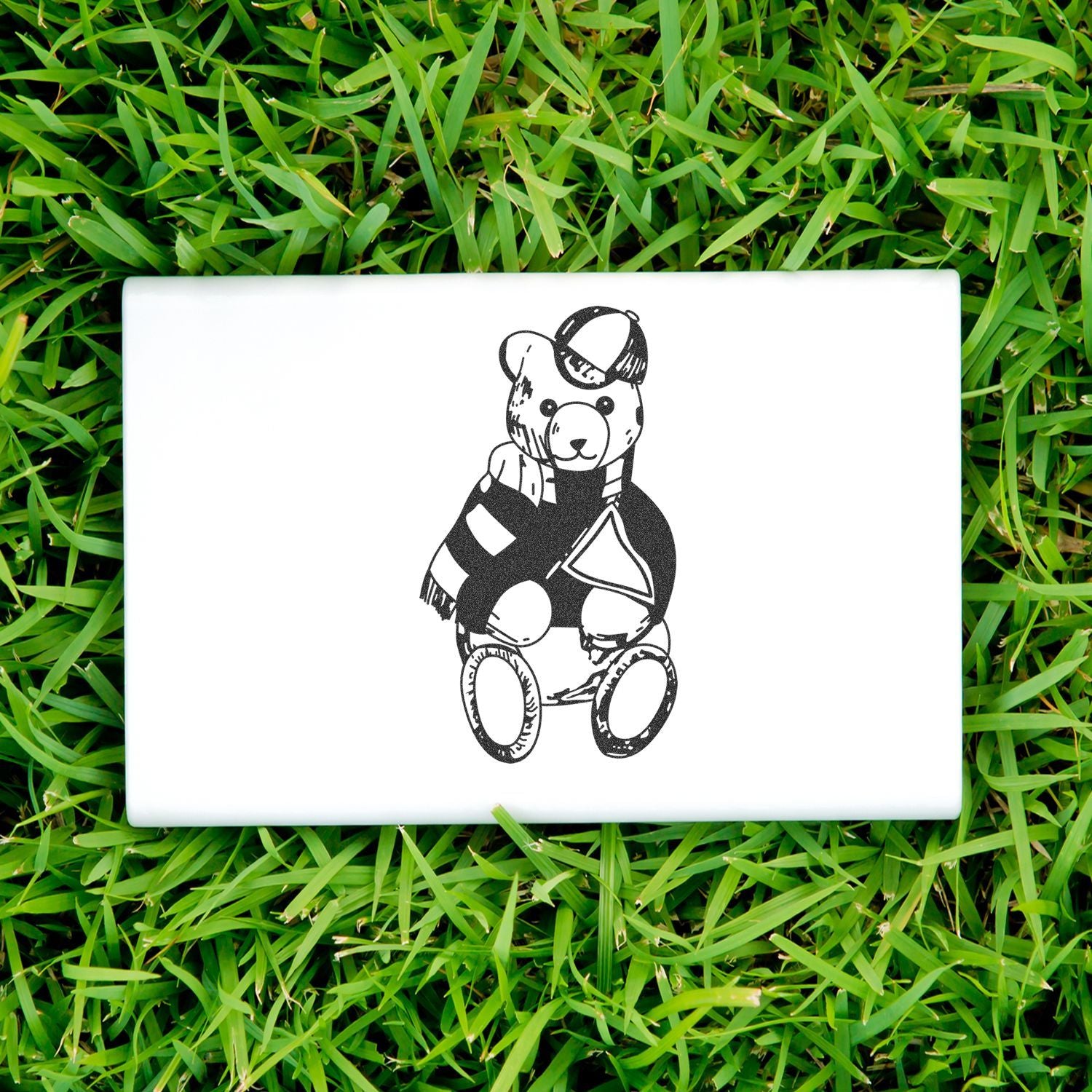 White ceramic tile with black teddy bear illustration on green grass, cute minimalist decor.