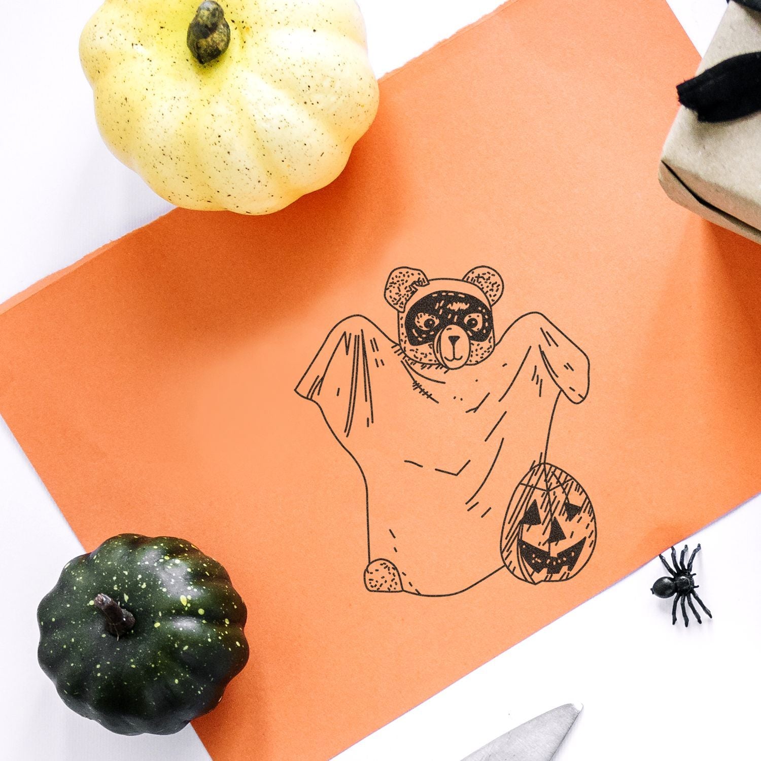 Halloween craft with spooky bear illustration on orange paper, surrounded by decorative pumpkins and a spider.
