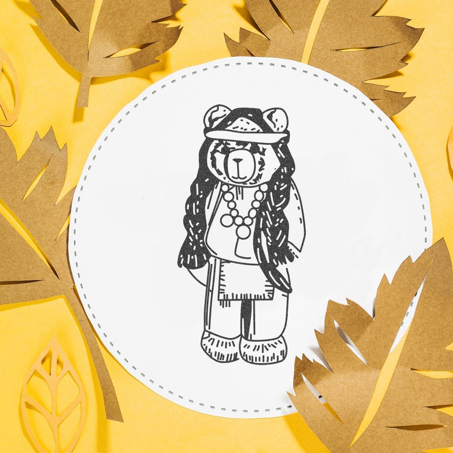 Cute paper bear illustration surrounded by autumn leaves on a yellow background, creative seasonal craft design.