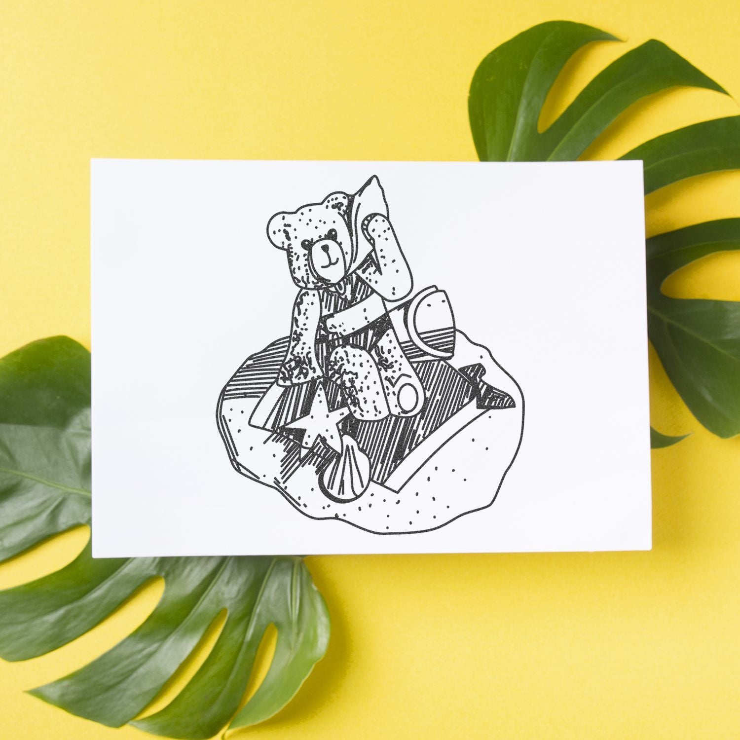 Minimalist teddy bear line art print on white card with tropical green leaves on a bright yellow background.