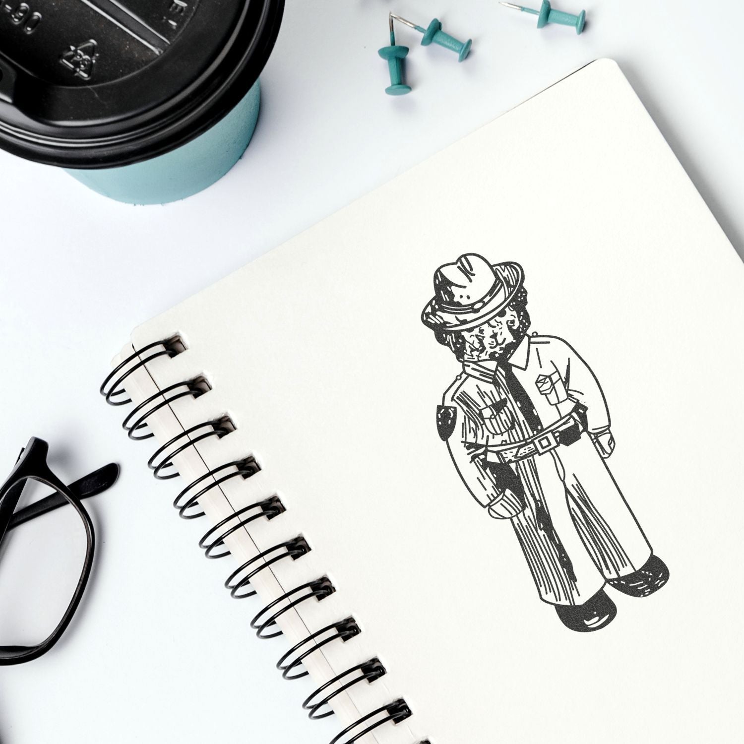 Spiral notebook with detective illustration on a clean desk, coffee cup and office accessories flat lay.