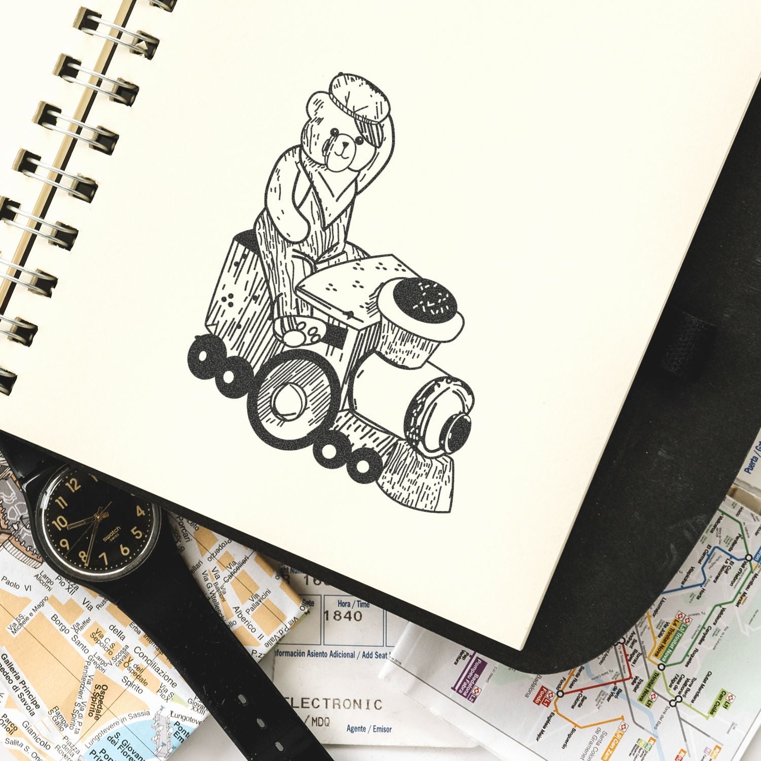 Sketchbook with hand-drawn teddy bear illustration on a toy train, surrounded by maps and a wristwatch.