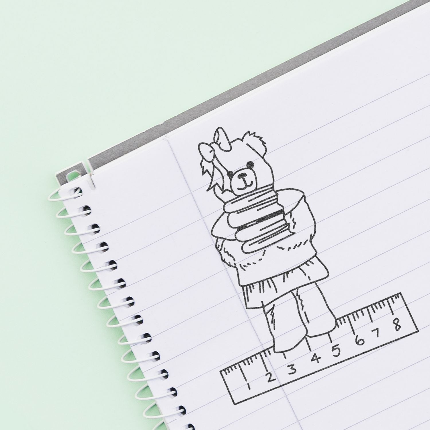 Cute llama sketch in a spiral notebook with ruler on a mint green background.