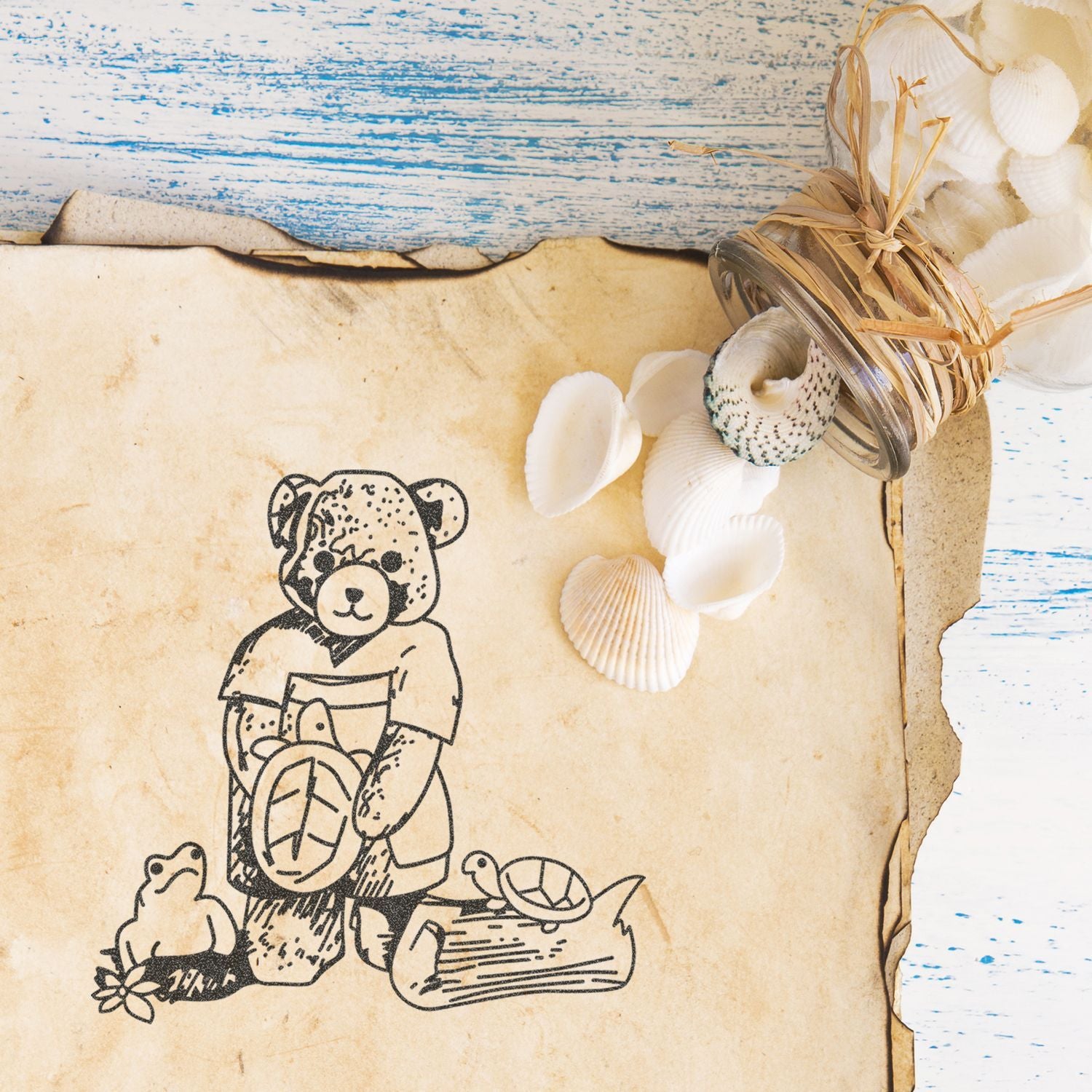 Vintage teddy bear drawing on aged paper with seashells and rustic beach decor on distressed blue wood background.