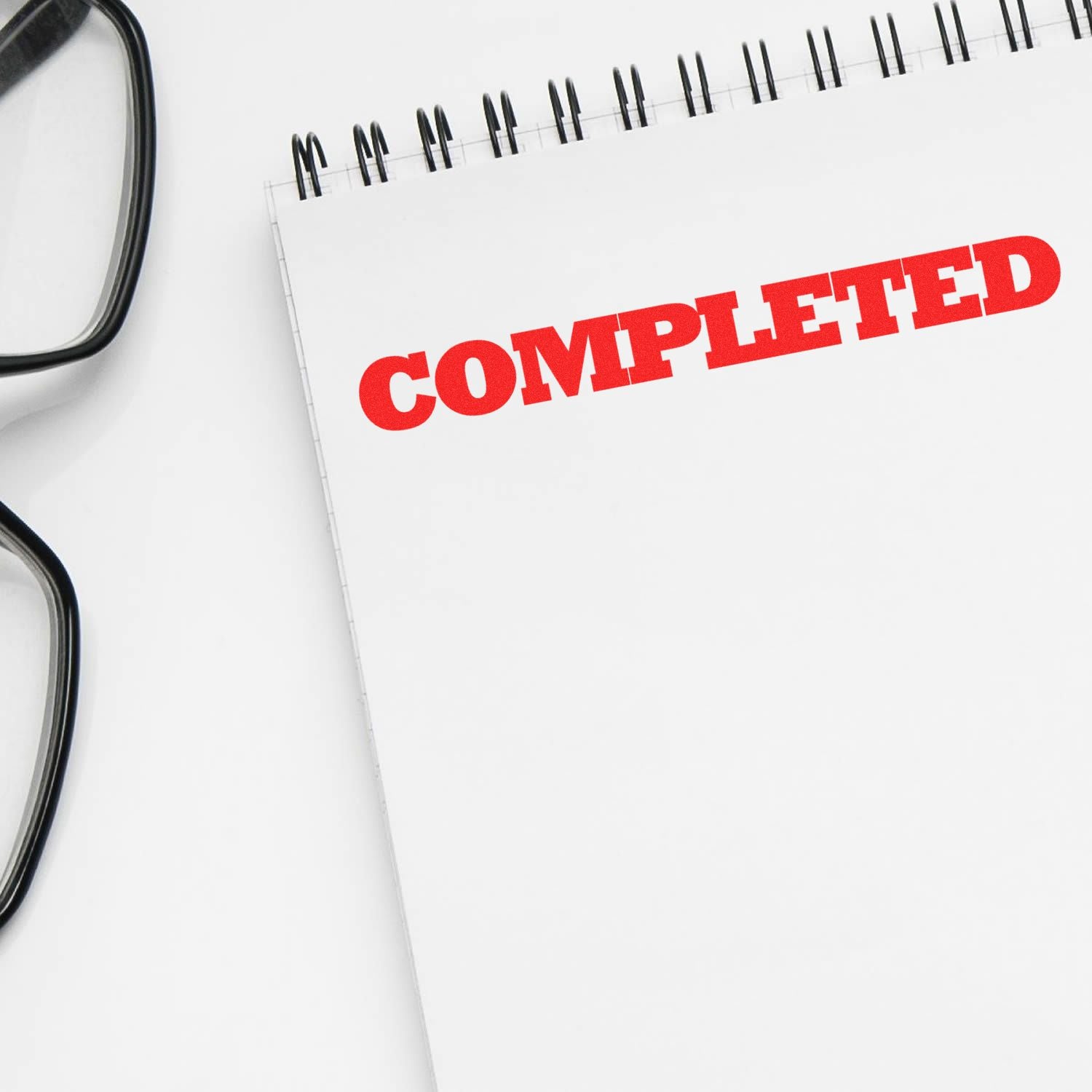 Blank spiral notebook with red COMPLETED stamp and eyeglasses, symbolizing finished tasks and project completion.