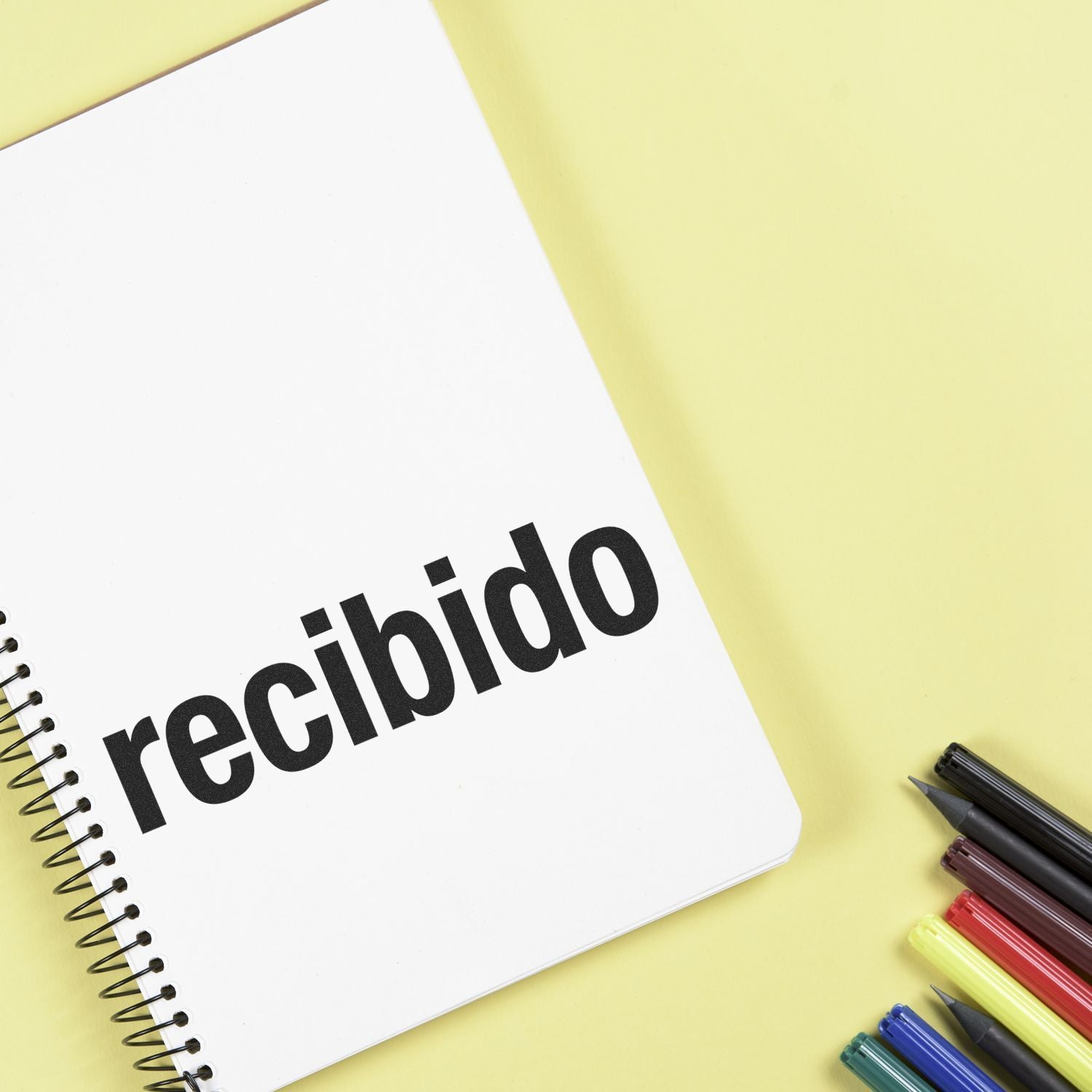 Recibido stamped notebook with colorful pens on yellow background, for tracking received messages and notes