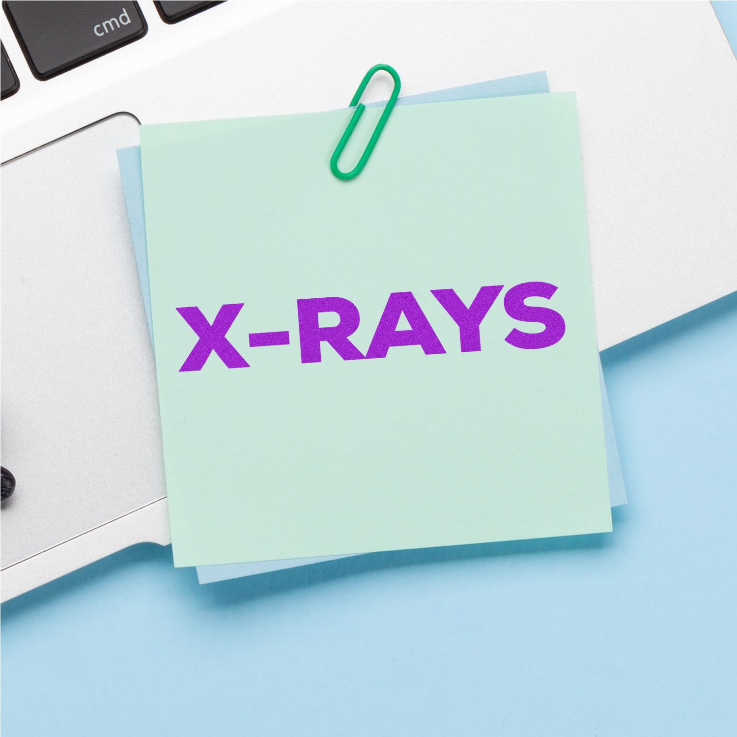 Sticky note labeled X-RAYS with paper clip and calculator keysmedical imaging radiology reminder for testing.