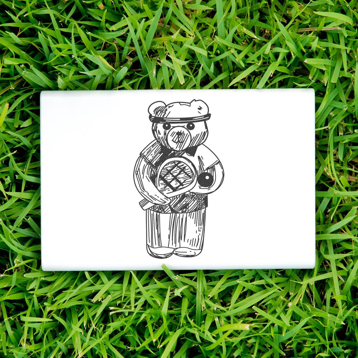 White laptop with a hand-drawn teddy bear illustration on green grass.