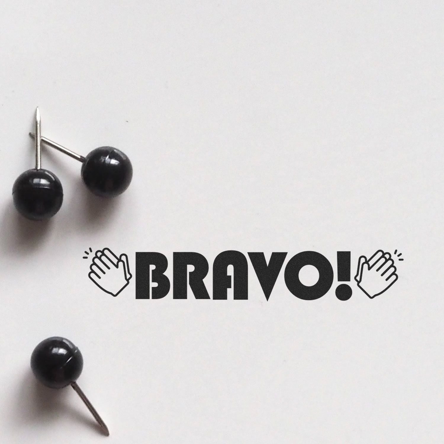Black pushpins spelling BRAVO! with applause hands icon on white background, celebrating success and positive feedback.