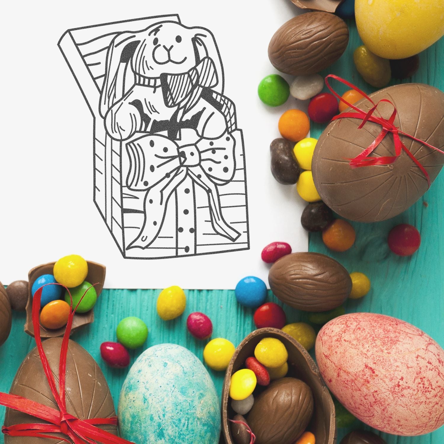 Colorful Easter chocolate eggs and candies arranged around a bunny gift box illustration on a turquoise background.