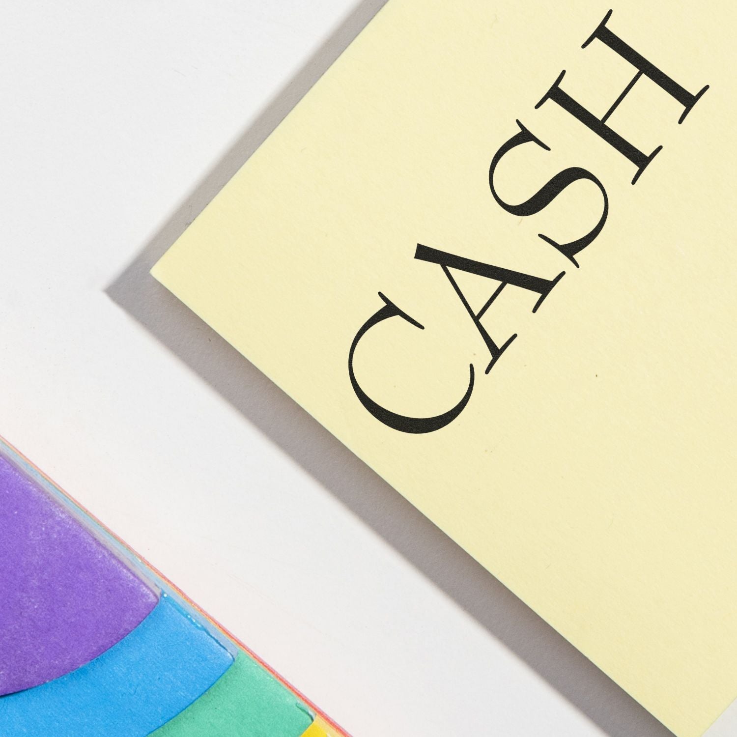Close-up of yellow cash note with bold black lettering on a white background, with colorful rainbow paper in the corner.