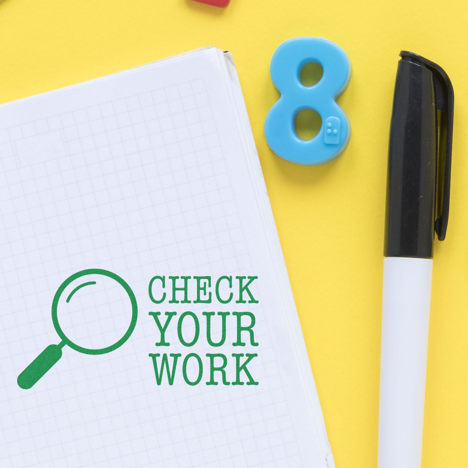 Top view of notebook with Check Your Work prompt, magnifying glass and pen for proofreading, writing, and editing student homework assignments.