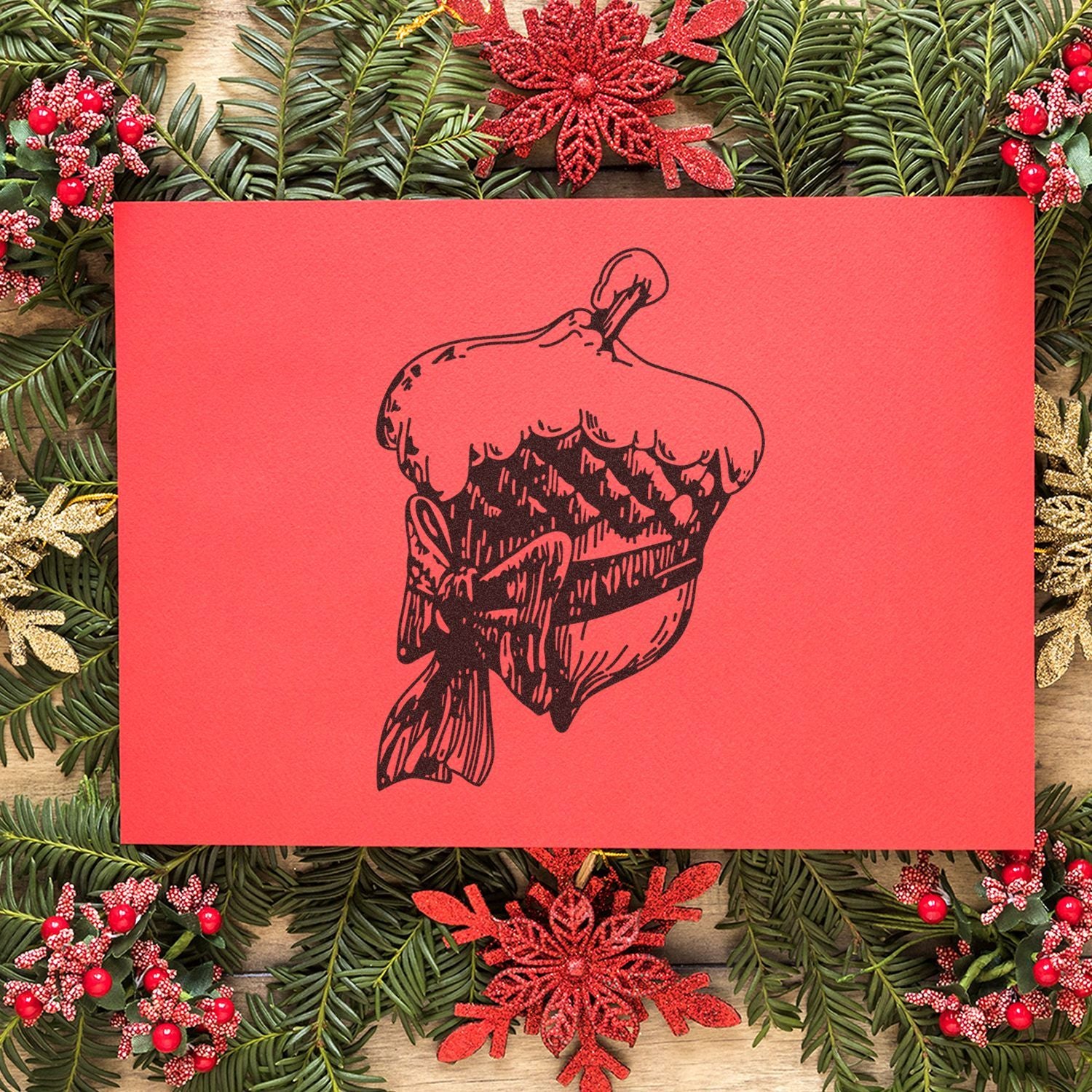 Festive red Christmas greeting card with black cupcake illustration, surrounded by holiday greenery, berries, and glitter snowflakes.
