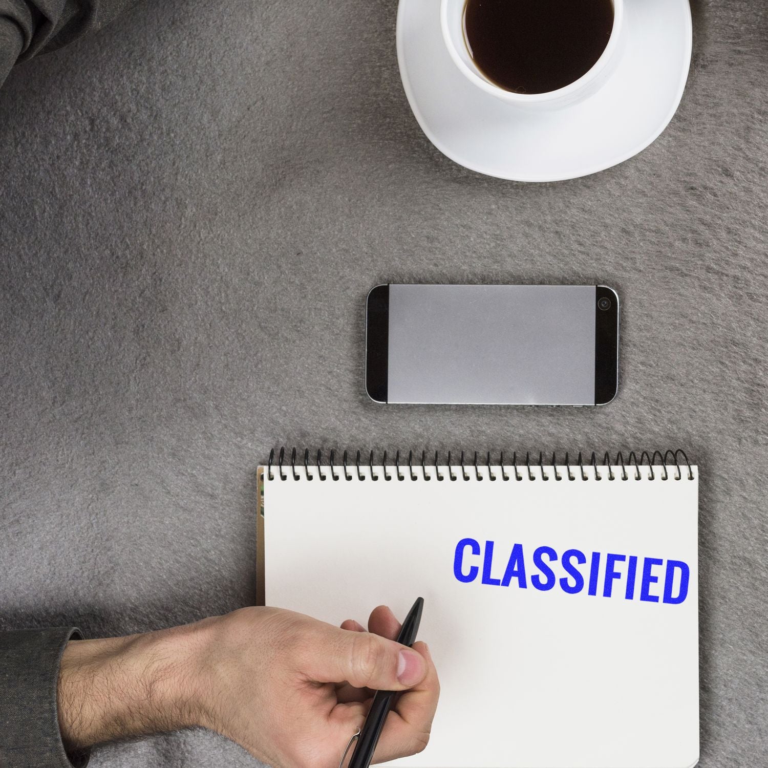 Hand writes on a notebook labeled CLASSIFIED, showing secure secret documents with coffee and phone on desk