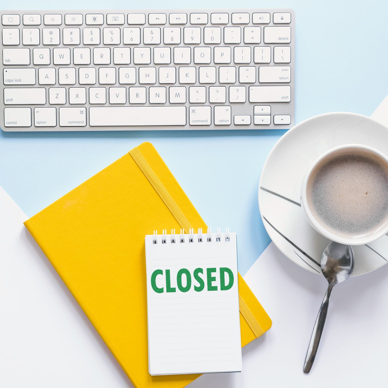 Desk workstation with CLOSED sign on notepad beside keyboard and coffee, showing a business closed for the day office hours notice.