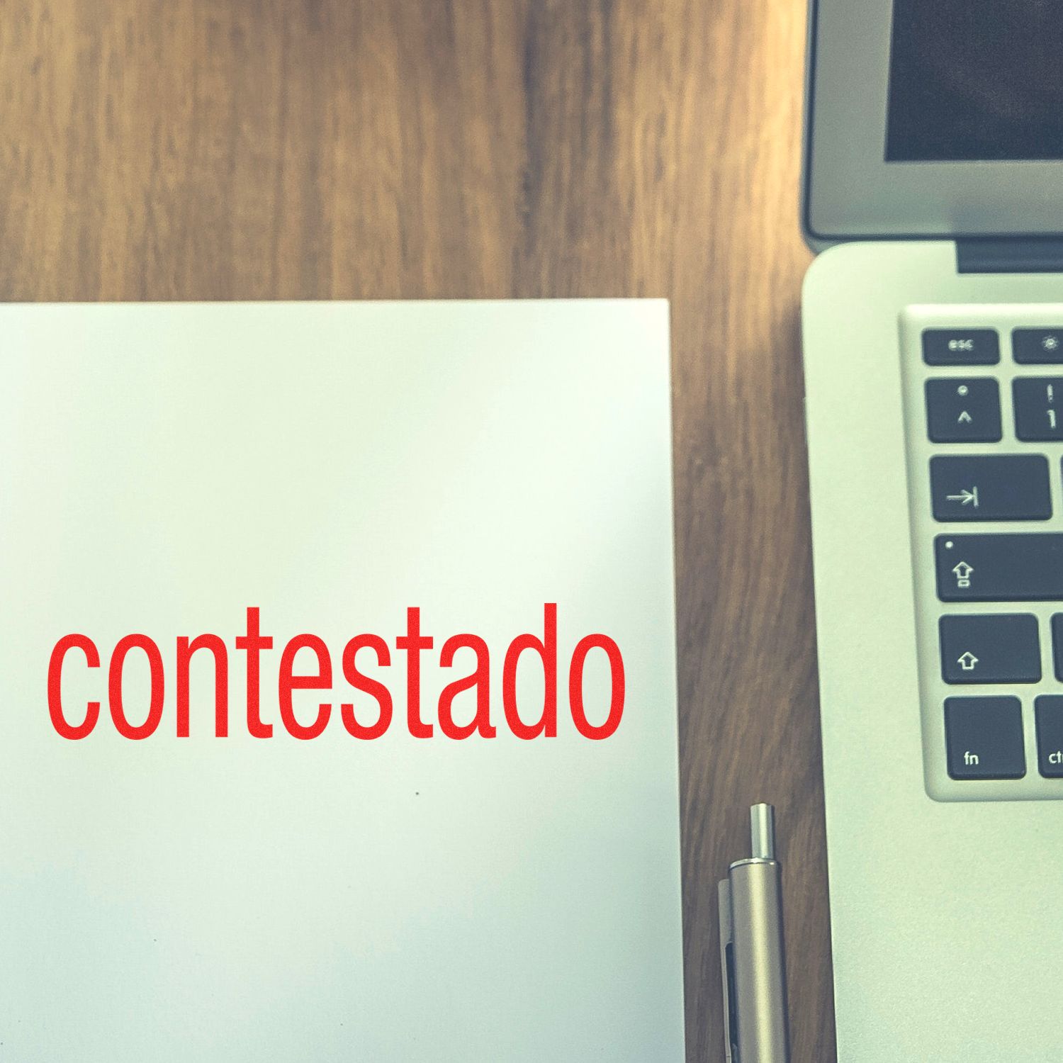 Documento con la palabra contestado junto a una laptop y un bolgrafo sobre escritorio de madera.