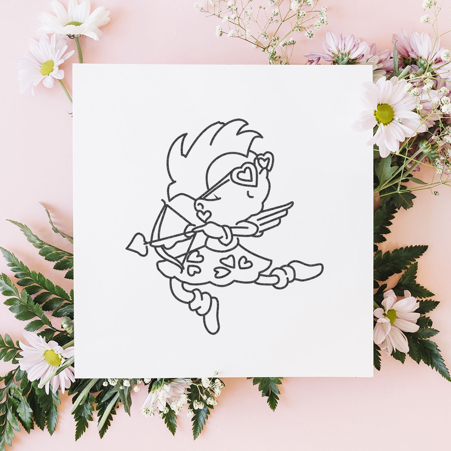 Cupid line art print on white paper surrounded by pastel flowers on a pink background, romantic Valentines Day floral flat lay.