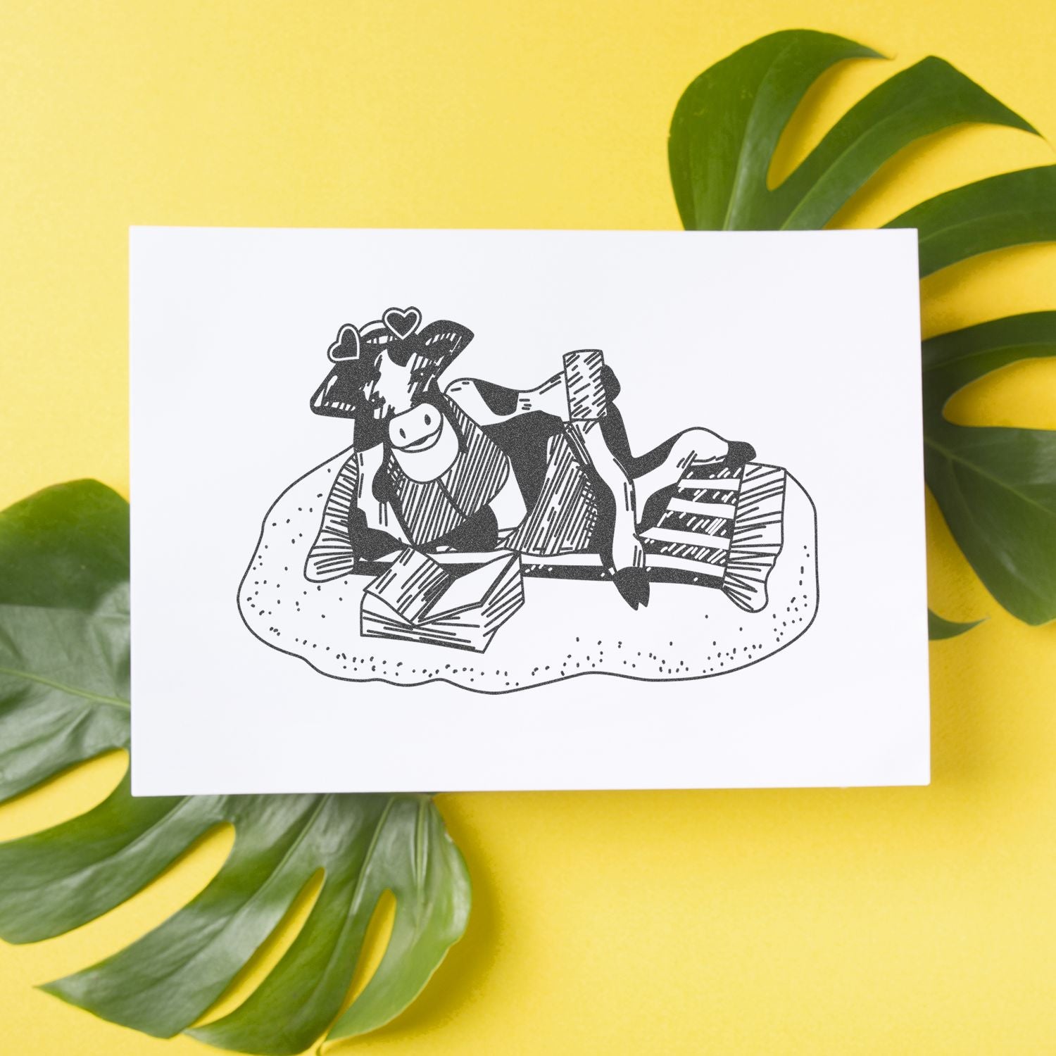 Hand-drawn cow illustration print on white card with tropical green leaves against a yellow background