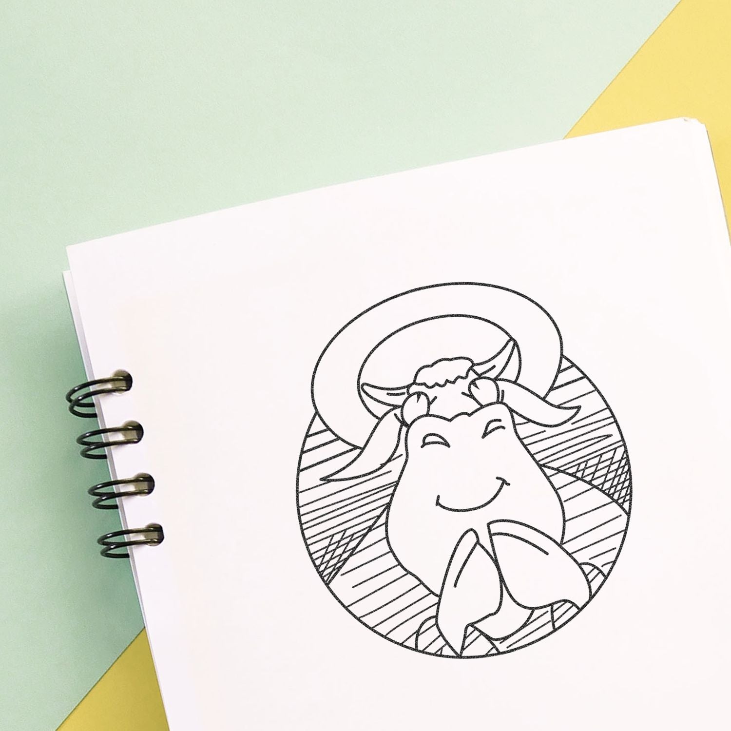 Cute cow coloring page in a spiral notebook on a pastel green and yellow background.
