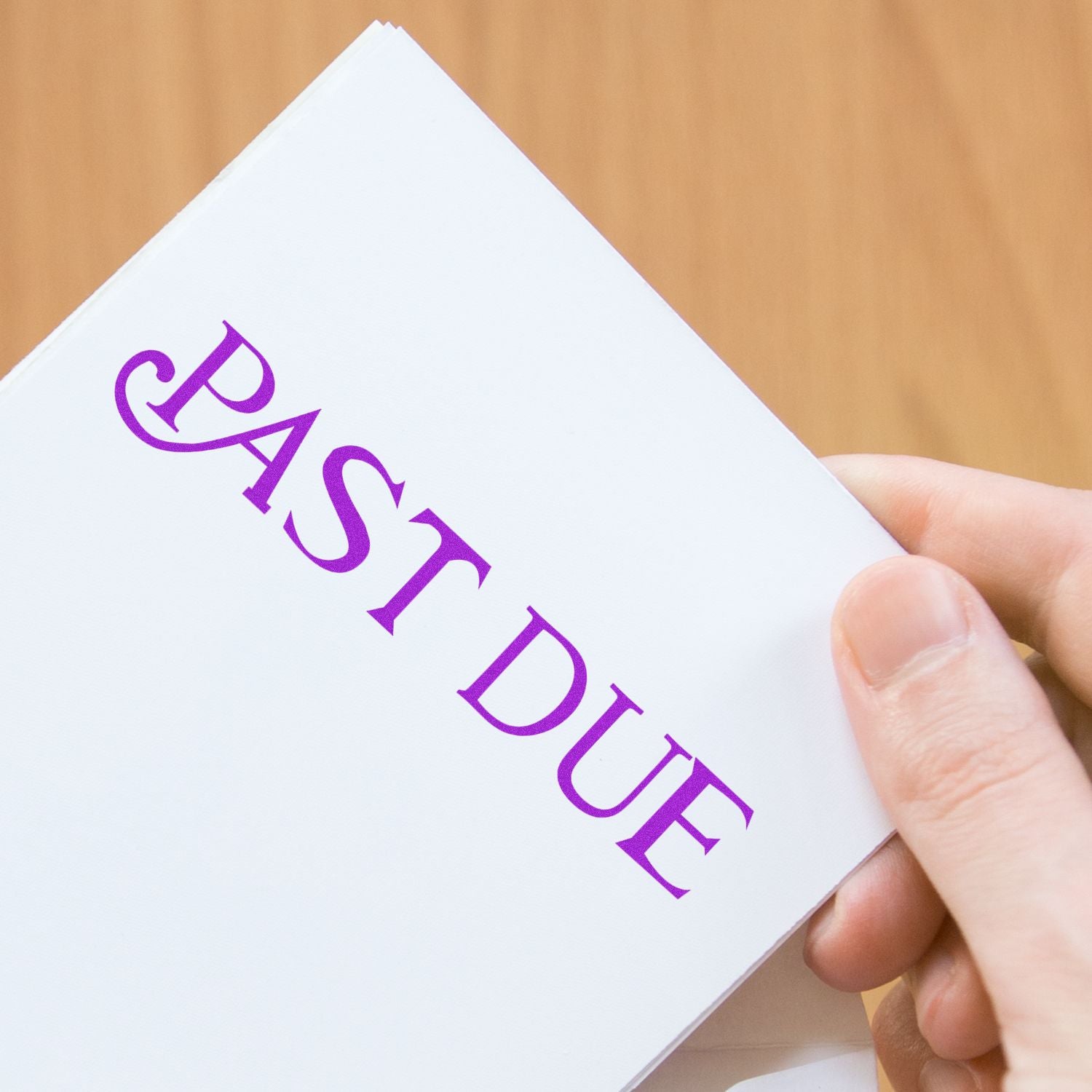 Hand holding a white past due notice with purple text on a wooden background