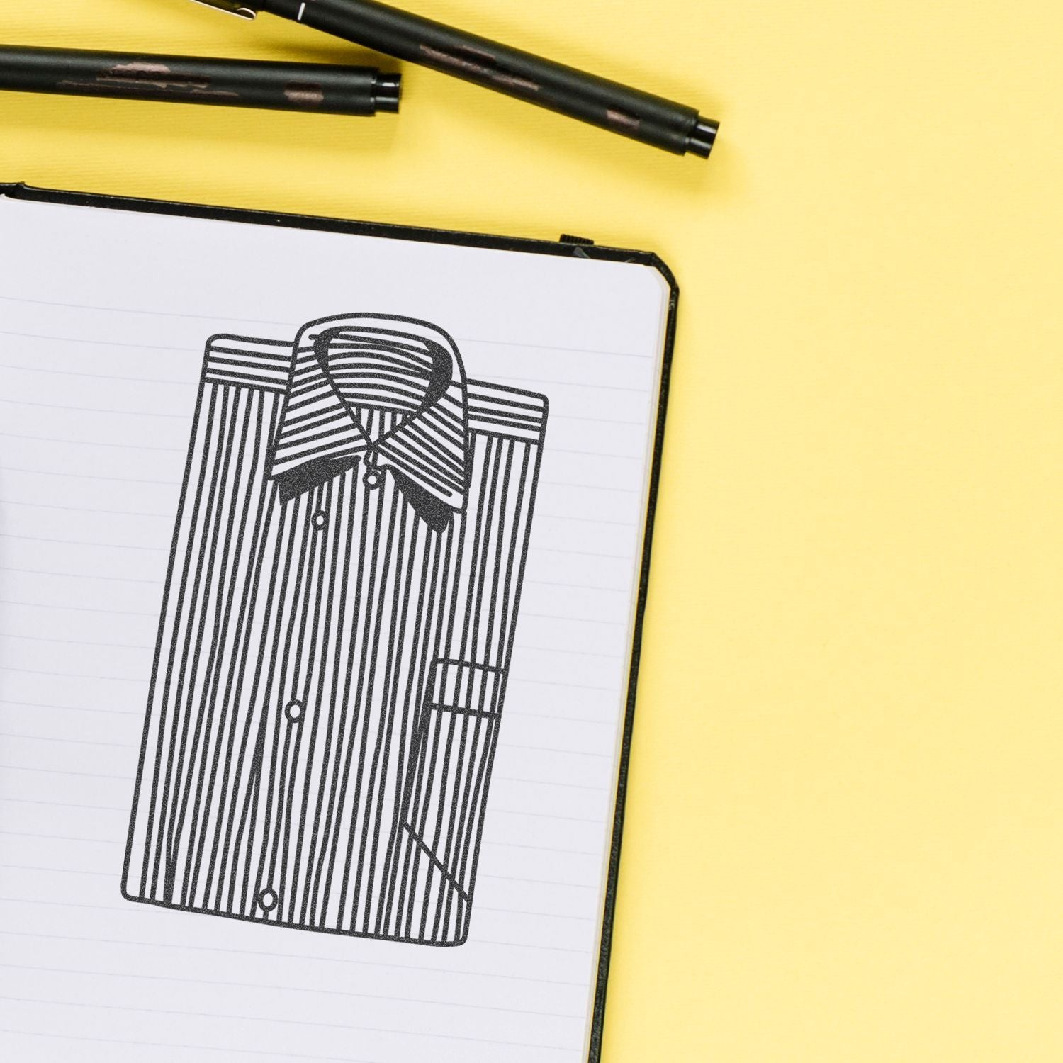 Fashion design sketch of a striped button-up shirt in a notebook on a yellow background.