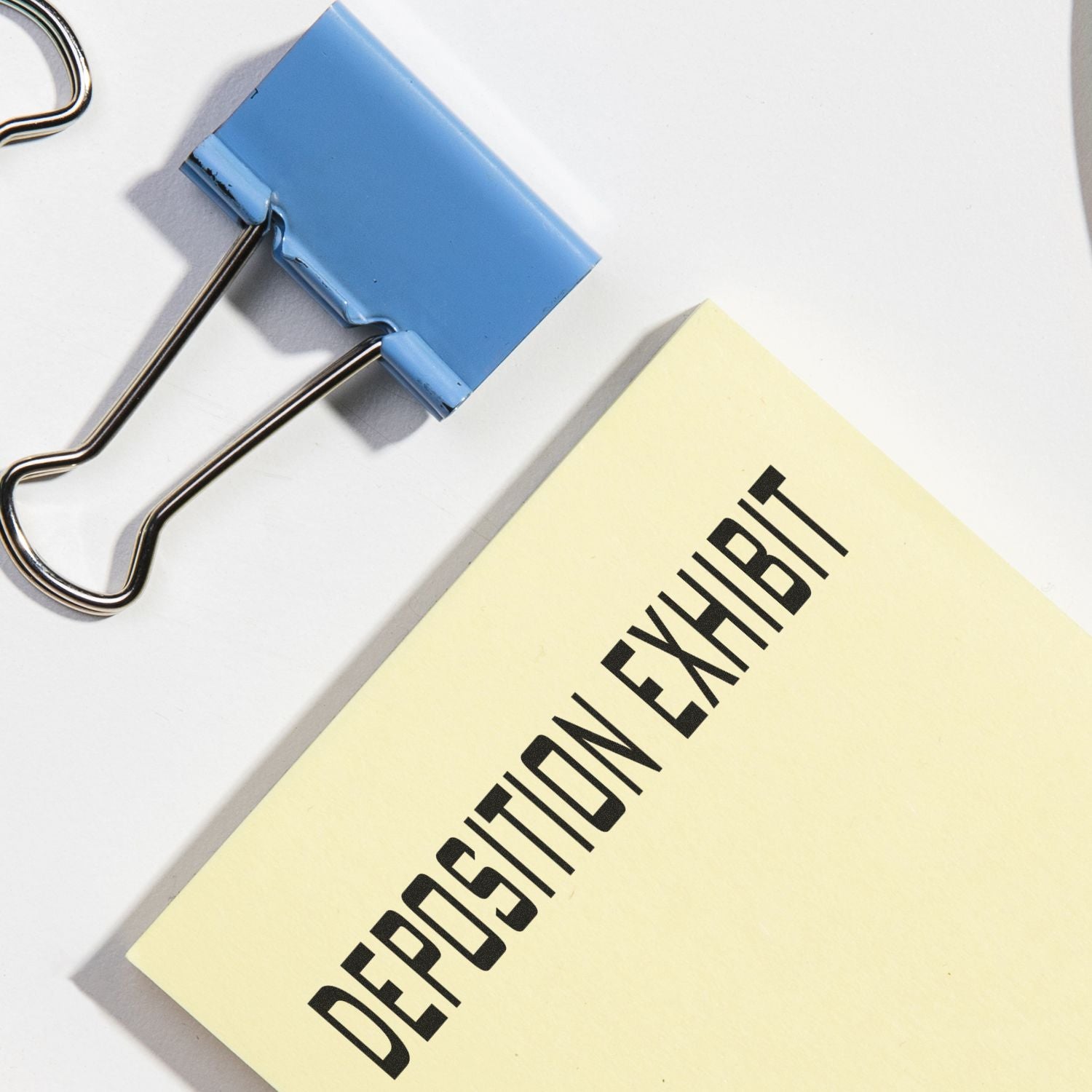 Blue binder clip holding a deposition exhibit document on a white background