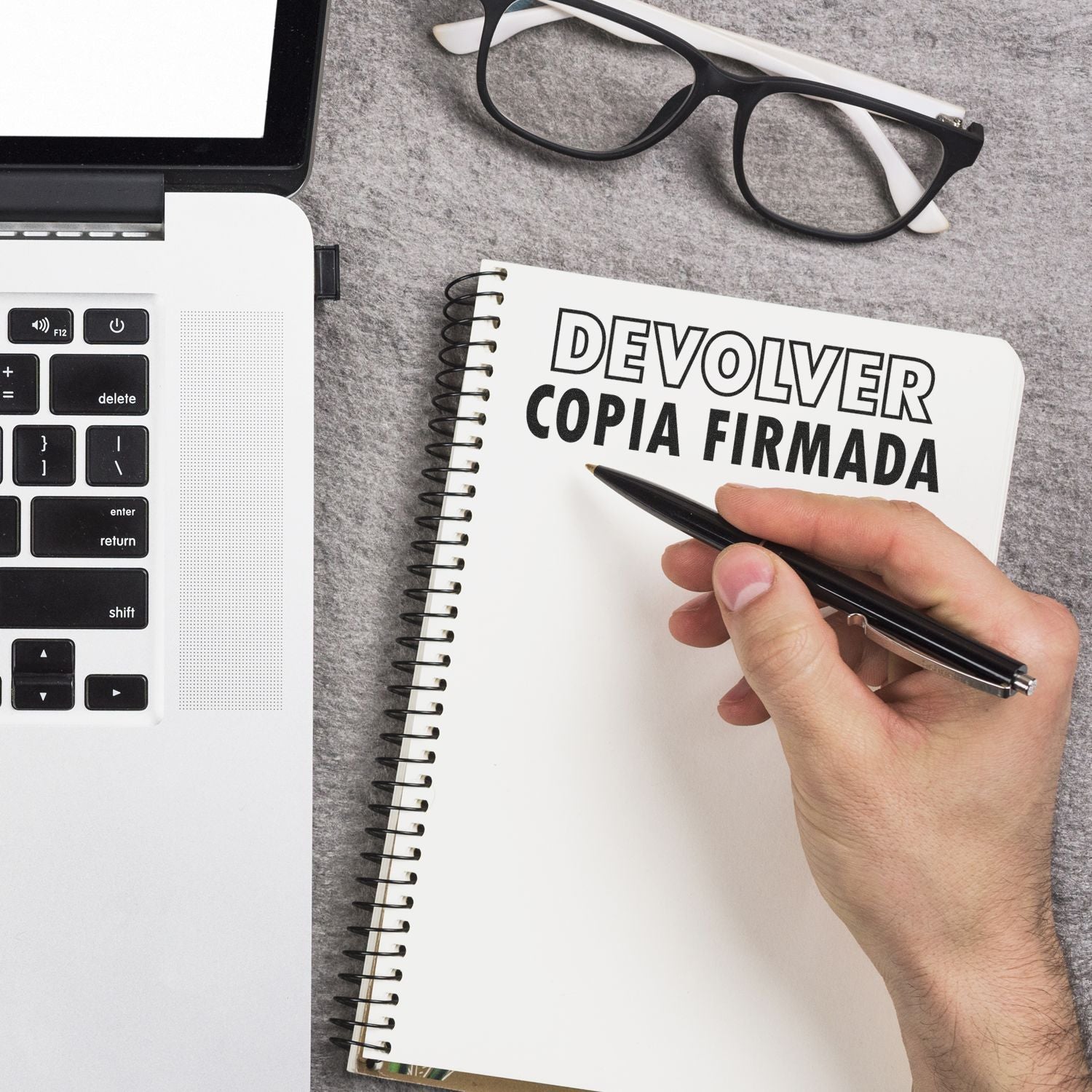 Mano firmando y escribiendo Devolver copia firmada en cuaderno, con calculadora y gafas, para documentos y trmites.