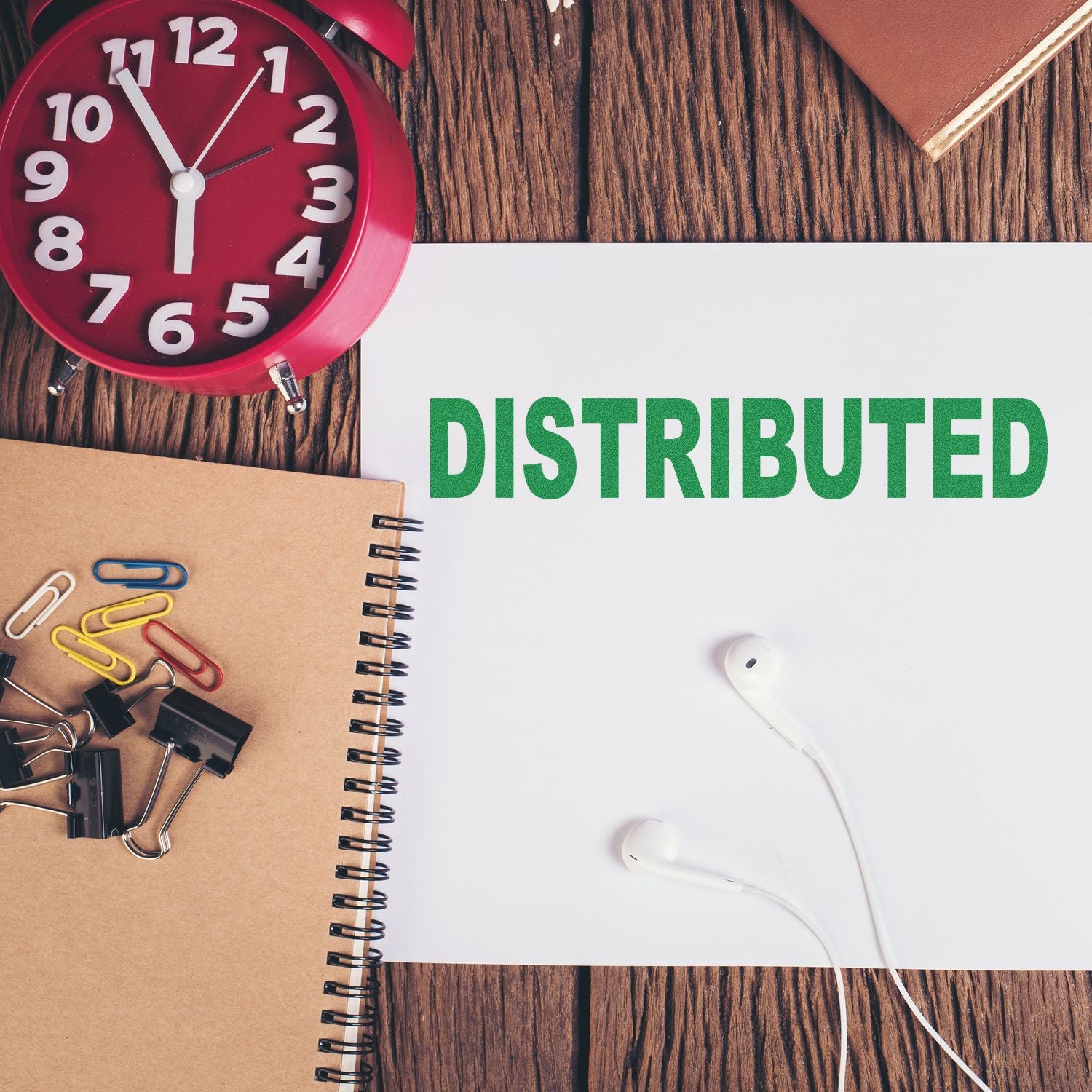 Distributed concept on desk with red clock, notebook, paper clips, and earbuds on wooden background.