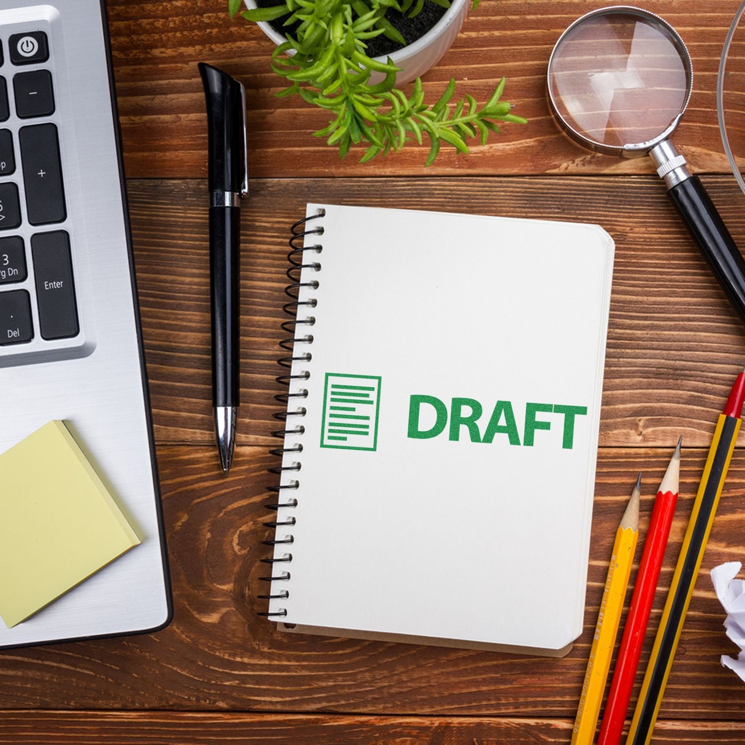 Draft planning notebook with DRAFT label, laptop, magnifying glass and pencils on wooden desk for writing and editing content ideas.