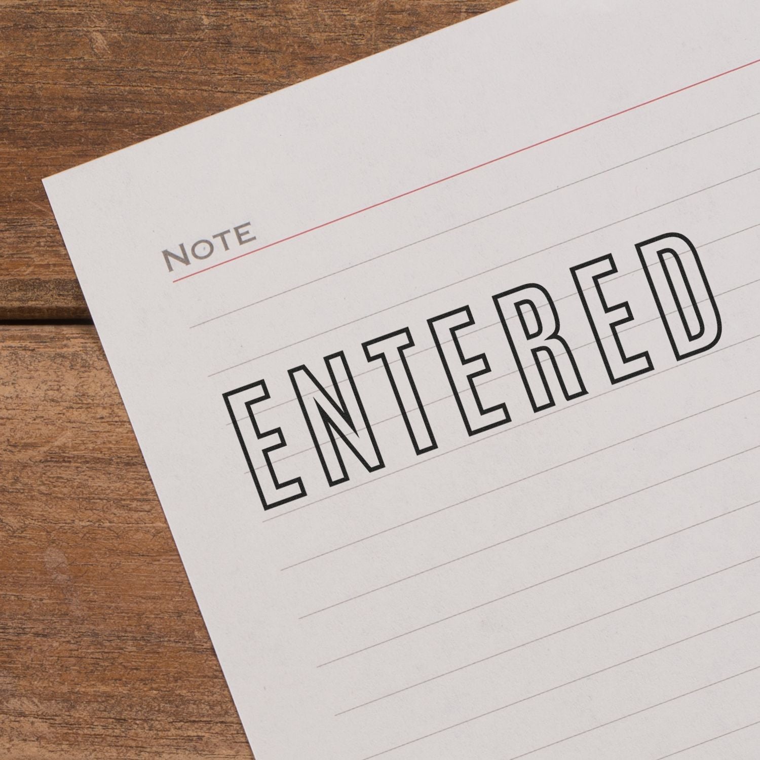 Close-up of lined note paper with the word ENTERED on a wooden desk.