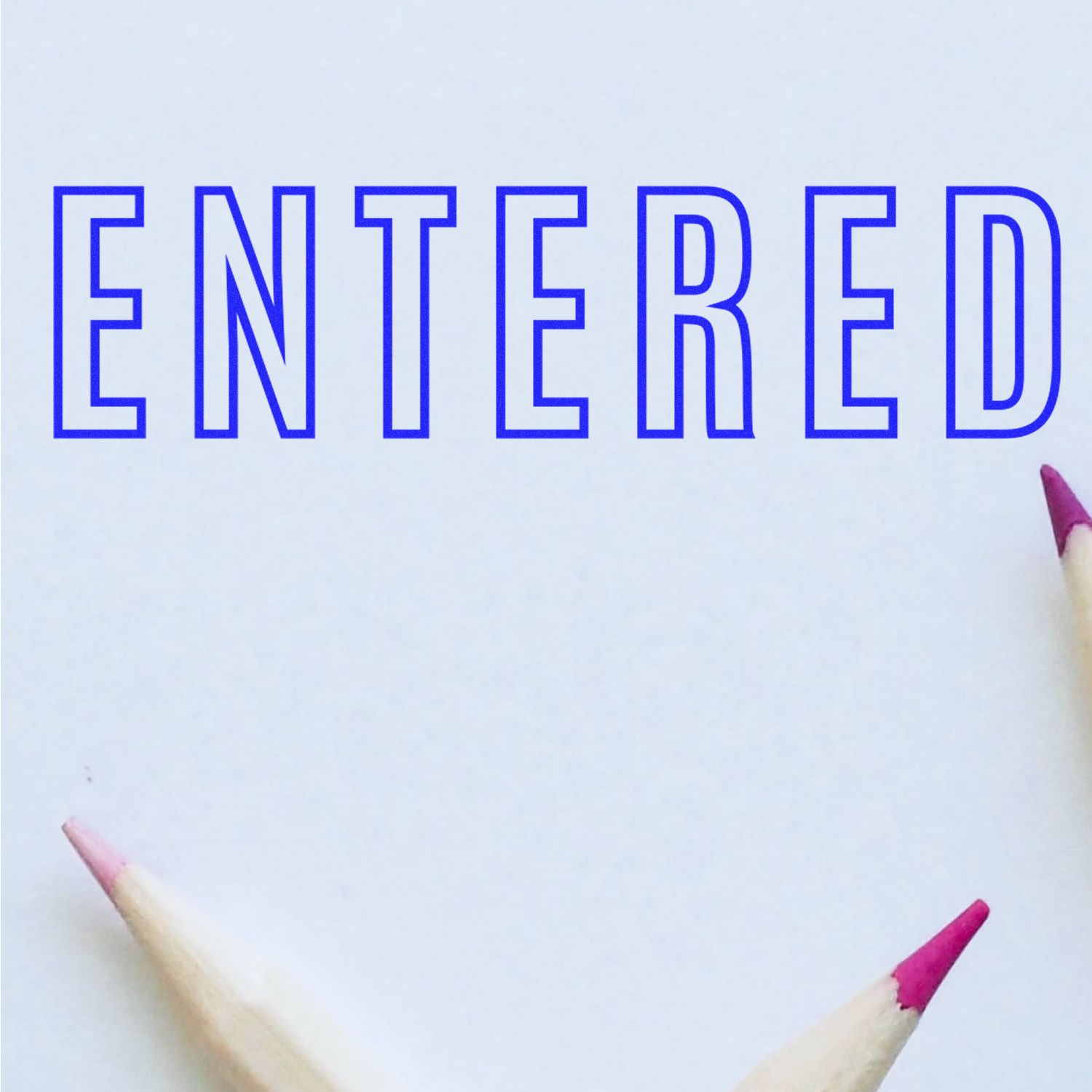 Blue outlined ENTERED text on white paper with colored pencil tips framing the corners, minimal flat lay design.