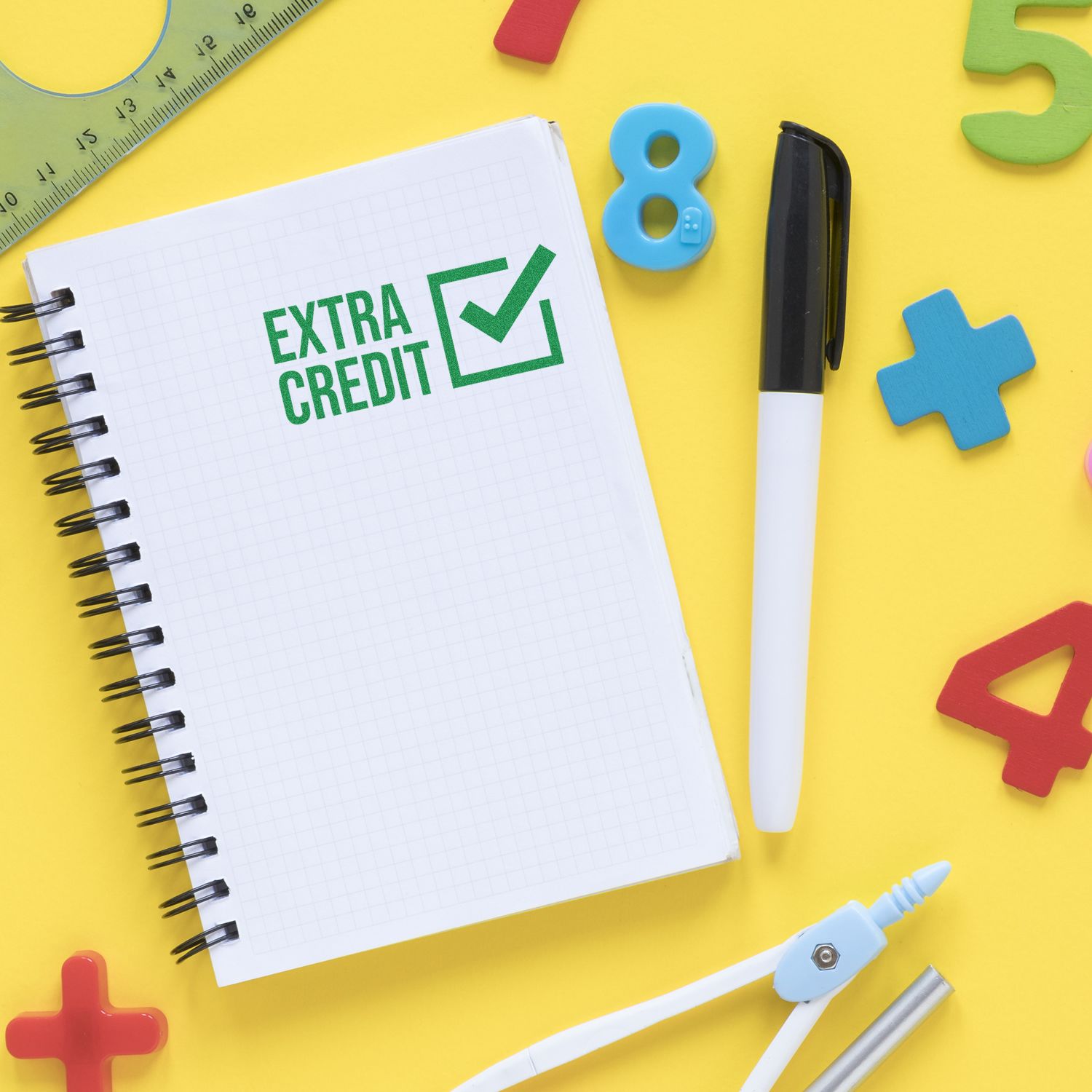 Extra credit text on a notebook surrounded by colorful school supplies on a yellow background.