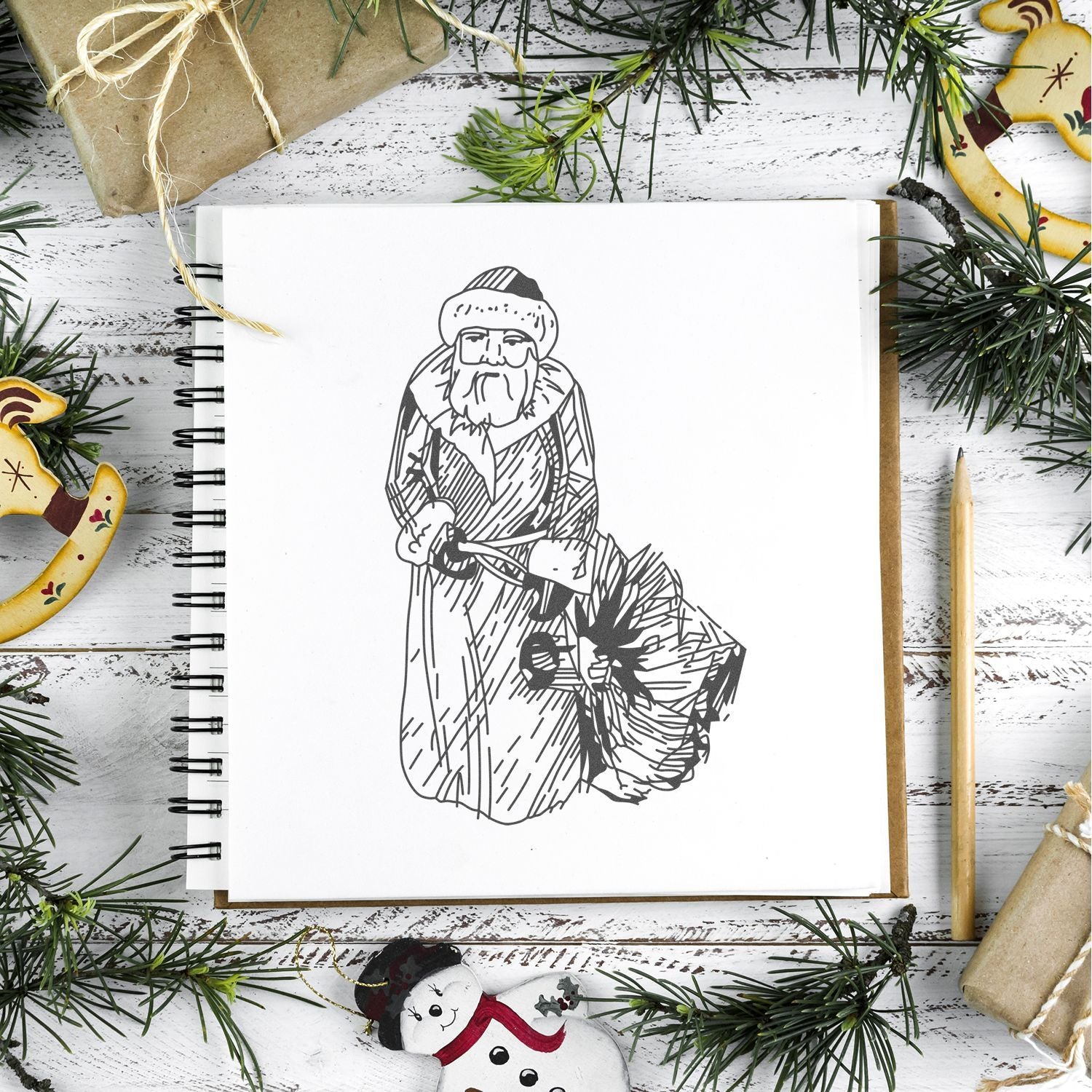 Festive Christmas sketchbook with Santa illustration, surrounded by pine branches, wrapped gifts, and holiday ornaments on a rustic wood table.