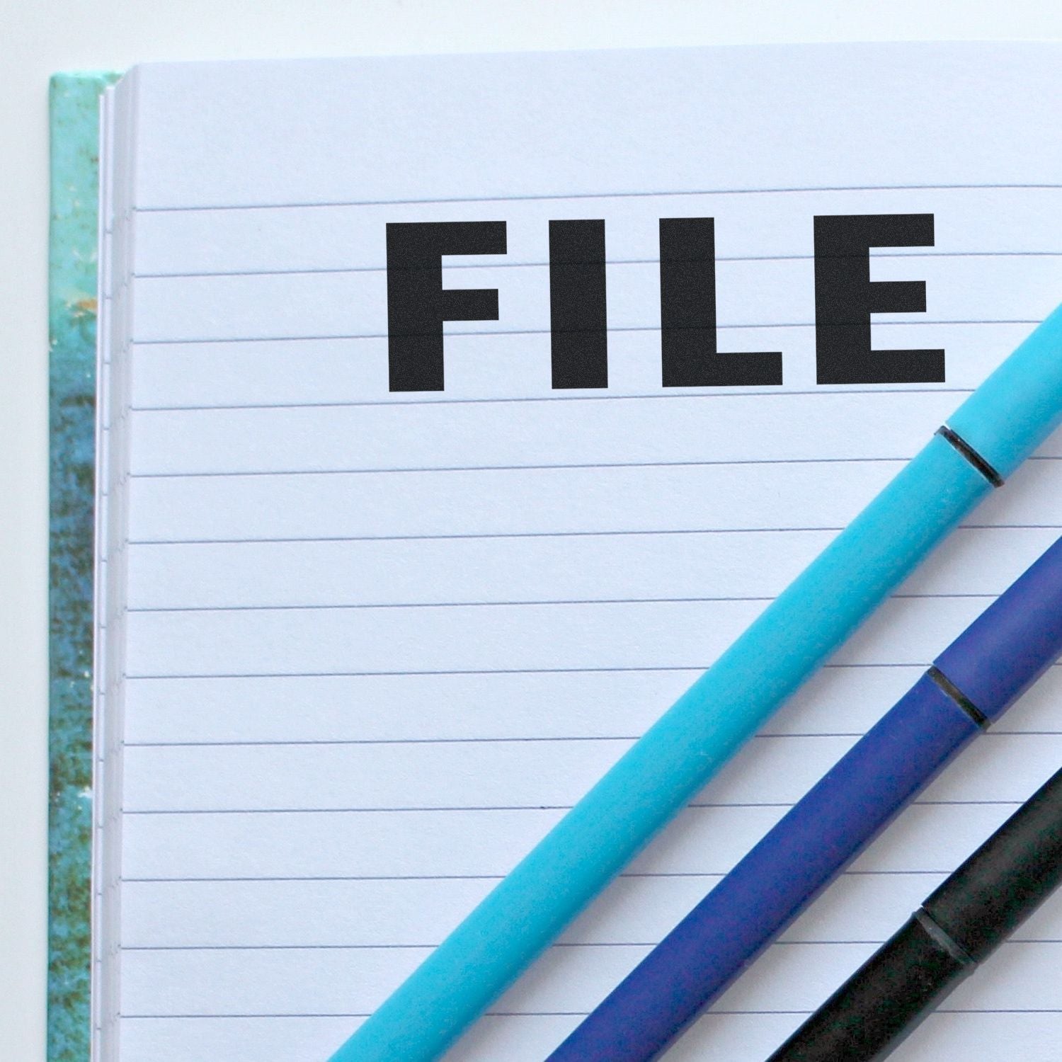 Notebook page labeled FILE with blue pens, representing document filing, organization, and productive writing.