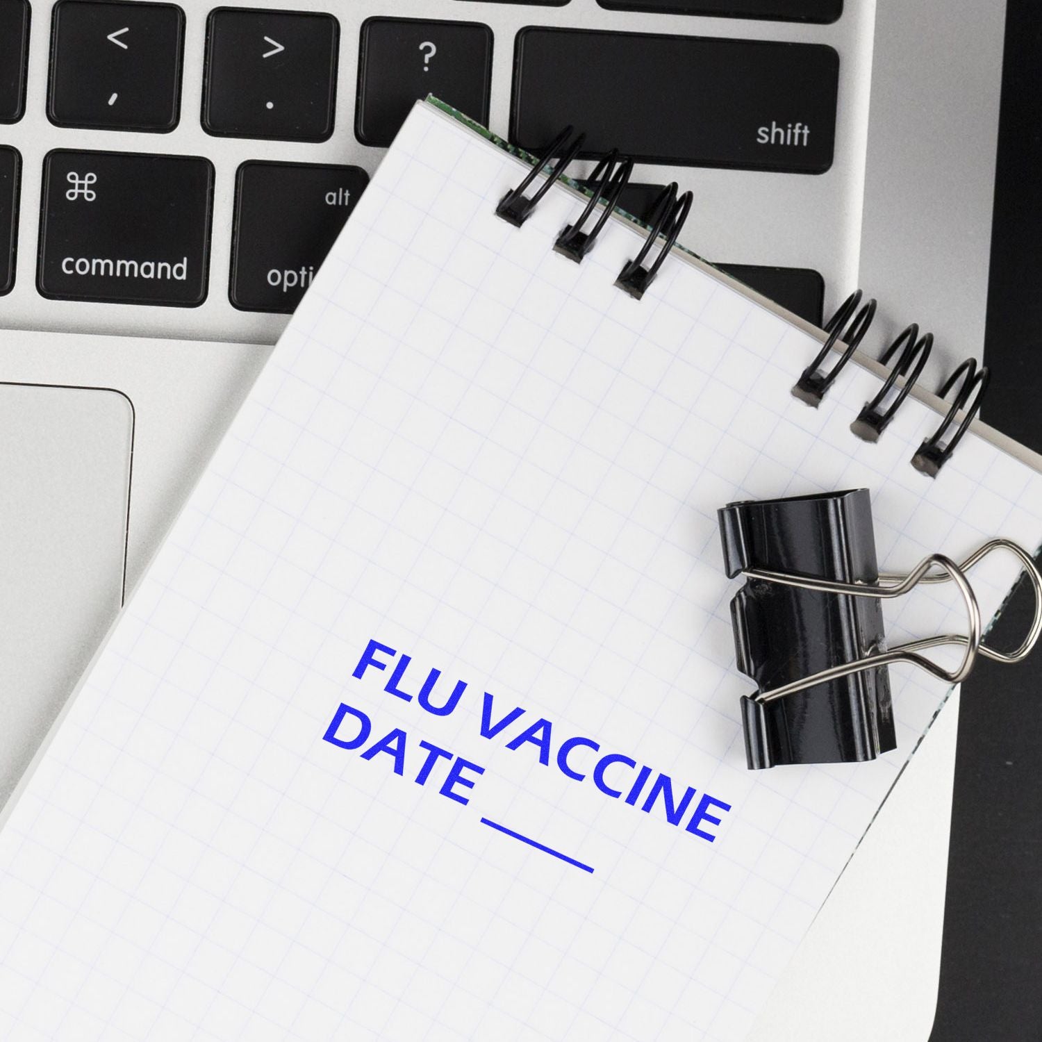 Notebook with flu vaccine date reminder on laptop keyboard, vaccination schedule concept.
