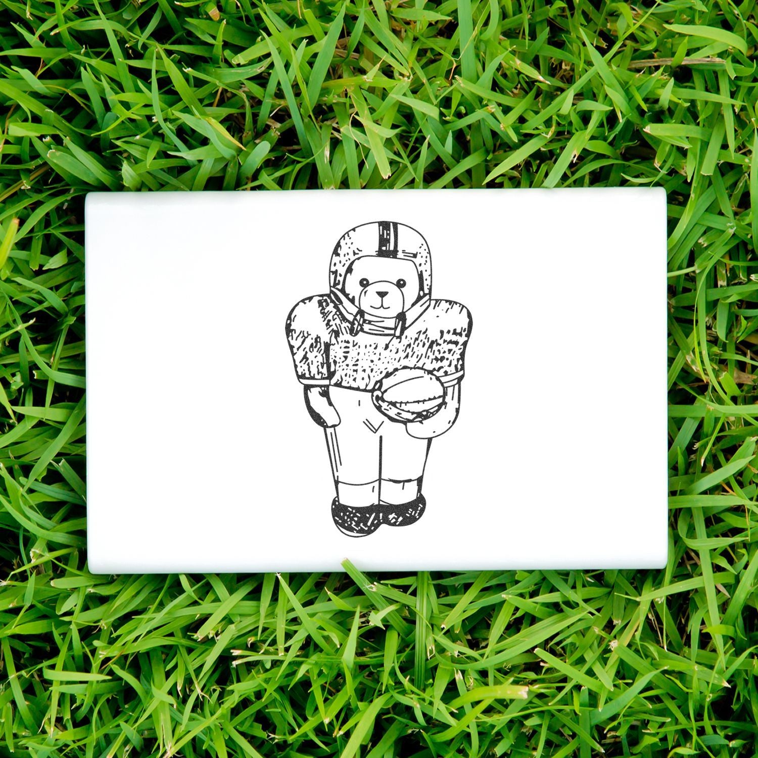 White laptop with a cute bear football player illustration on the lid, placed on green grass.