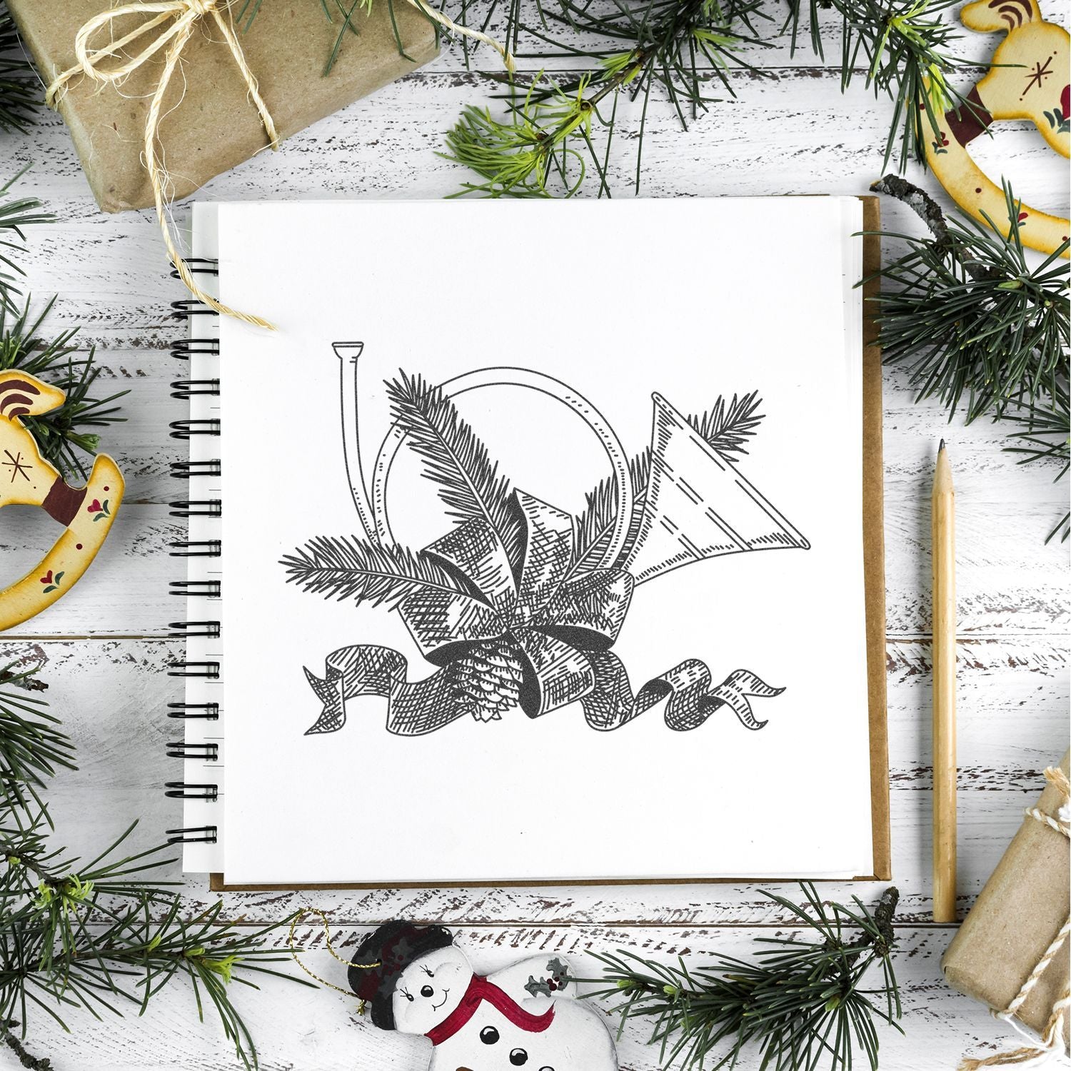 Holiday sketchbook with vintage Christmas ornament drawing, pine branches, wrapped gifts, and pencil on rustic white wood background.