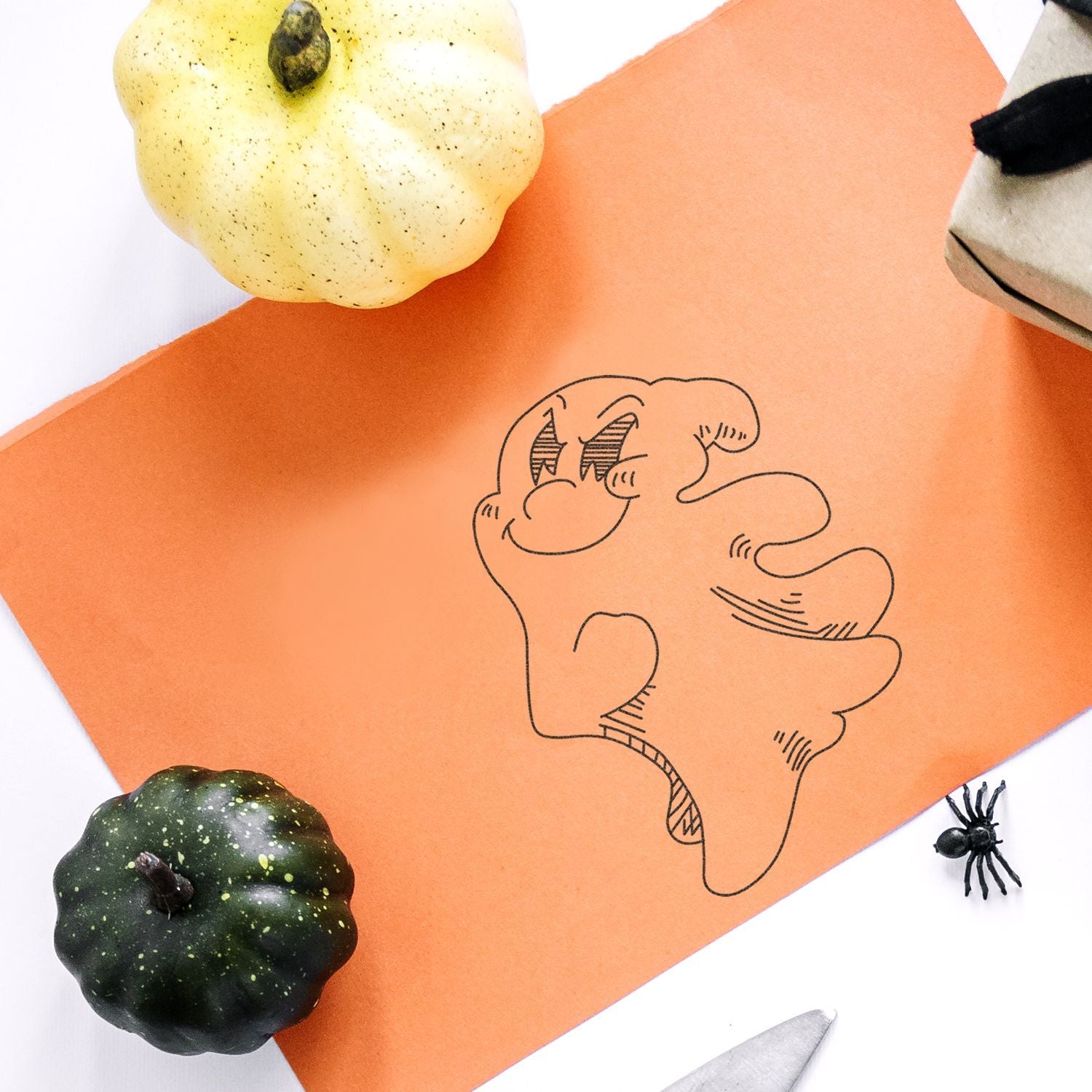 Halloween craft flat lay with pumpkins, spider, and spooky doodle on orange paper