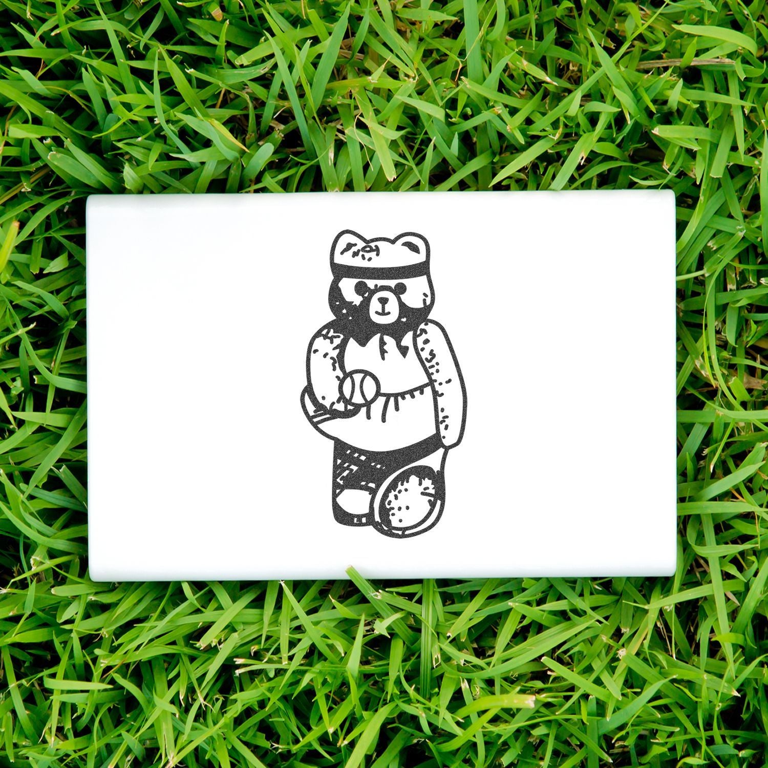 Black bear illustration on a white laptop cover placed on green grass.
