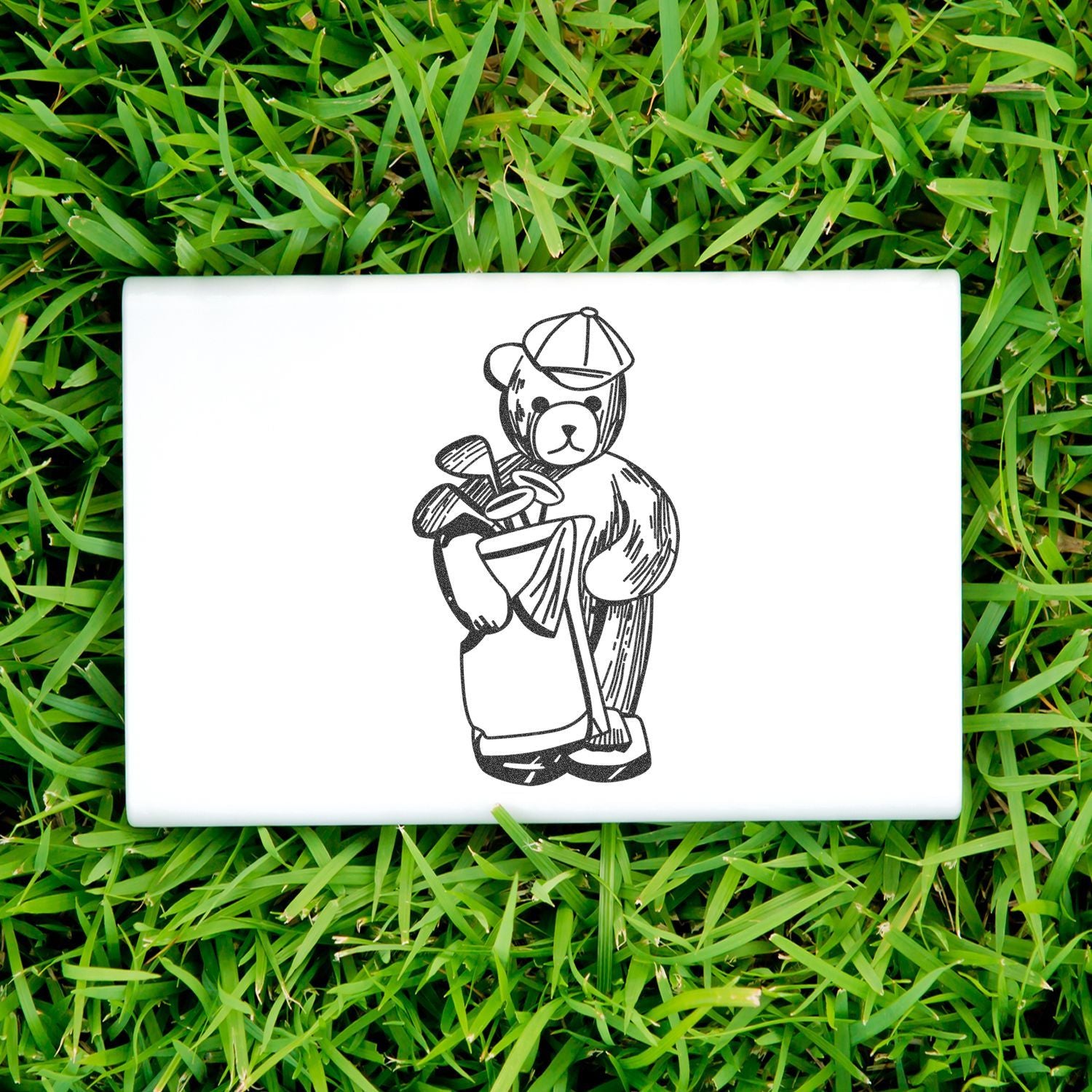 White golf-themed plaque with a teddy bear holding golf clubs, displayed on green grass.